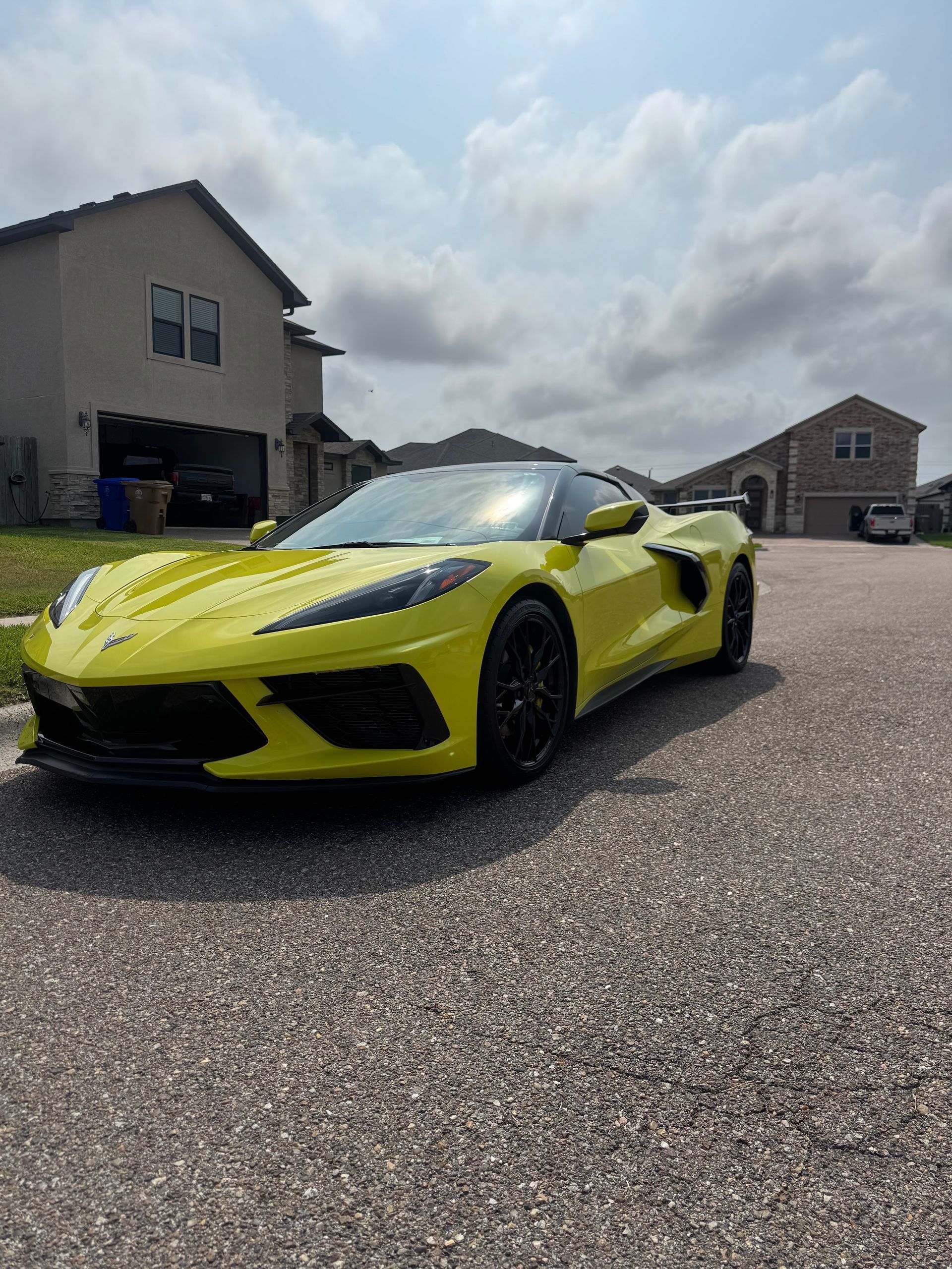 Yellow sports car parked on a residential street under a partly cloudy sky