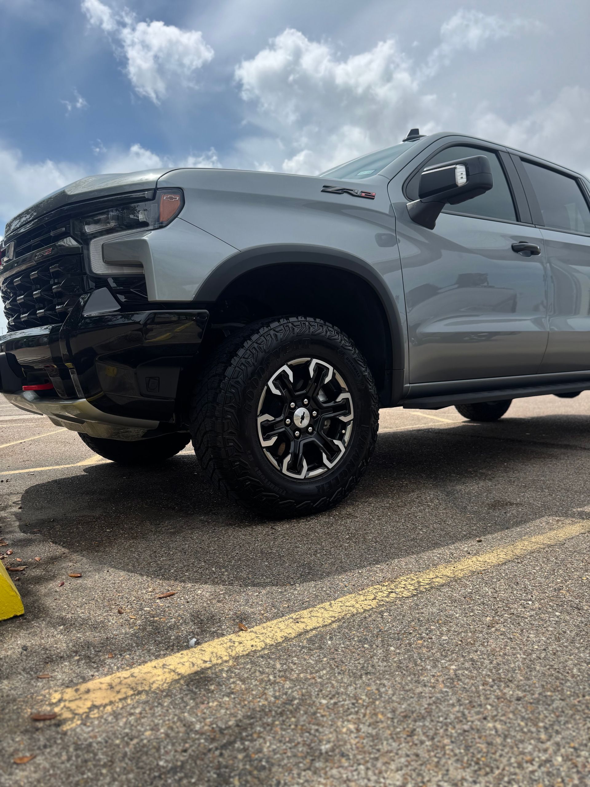 Silver pickup truck parked in a lot under a cloudy sky, side view from a low angle