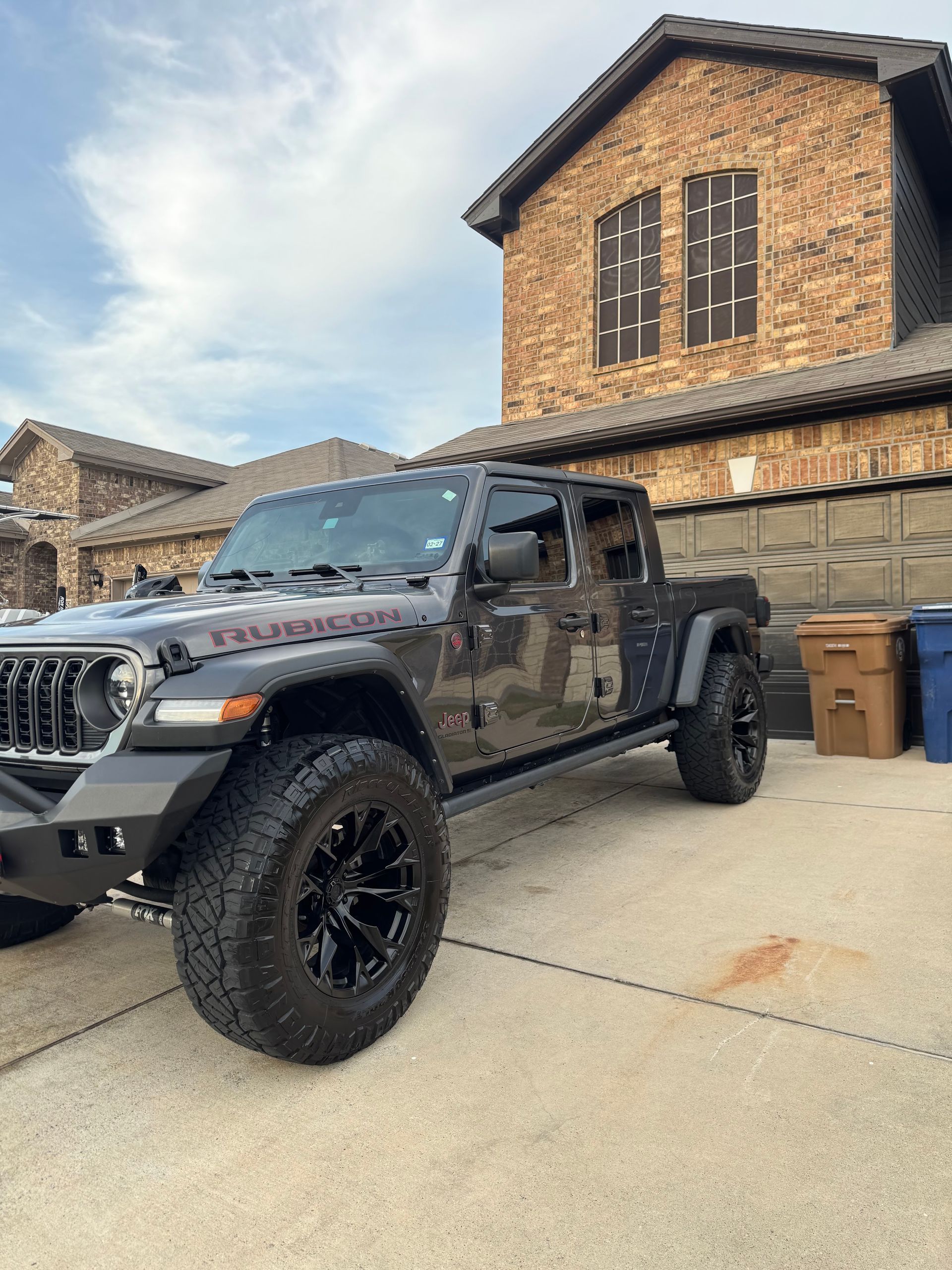 Black Jeep Gladiator in a driveway in front of a brick house under a partly cloudy sky