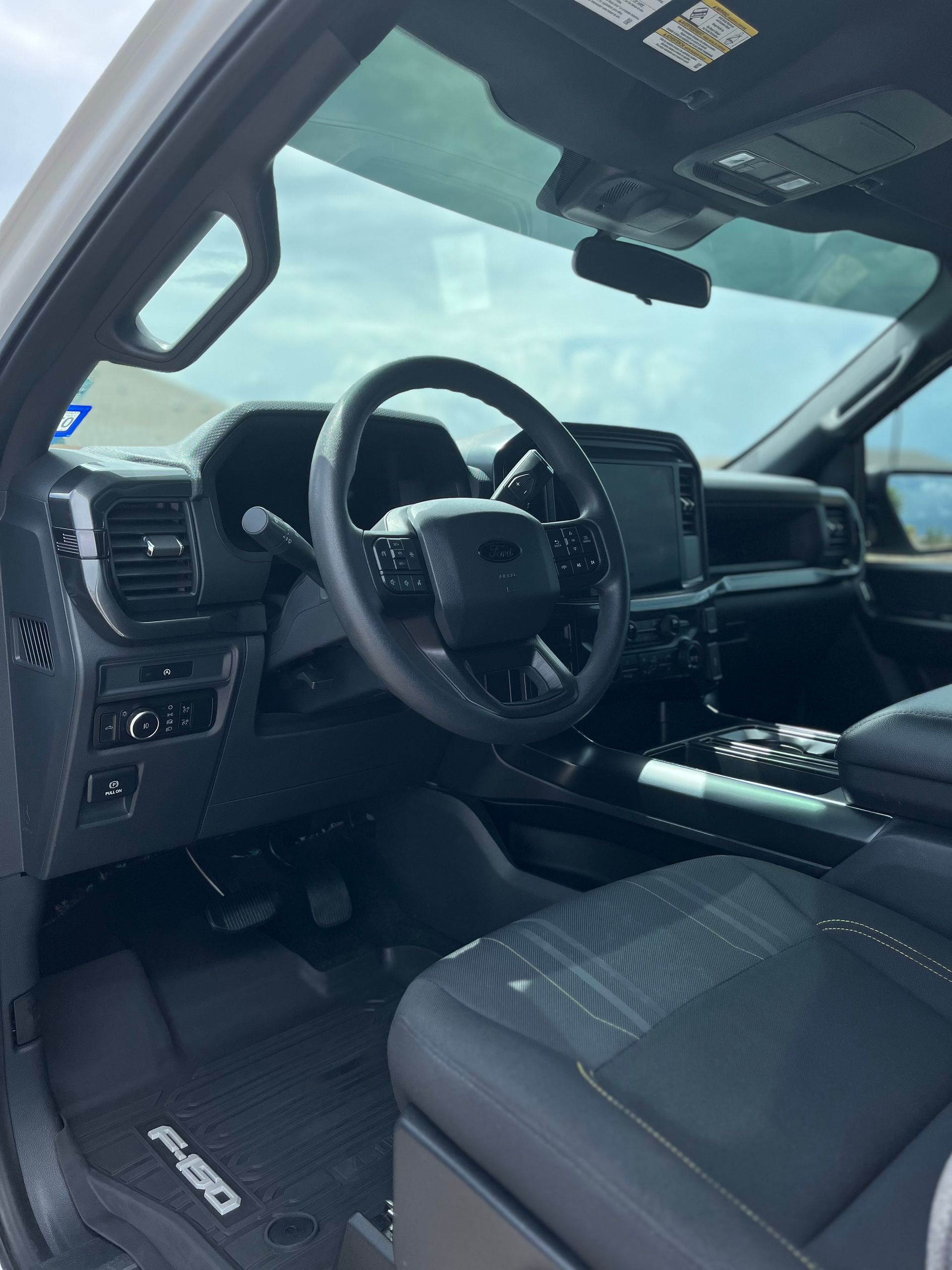 Truck interior with black seats, steering wheel, dashboard, and sunroof under a bright sky.