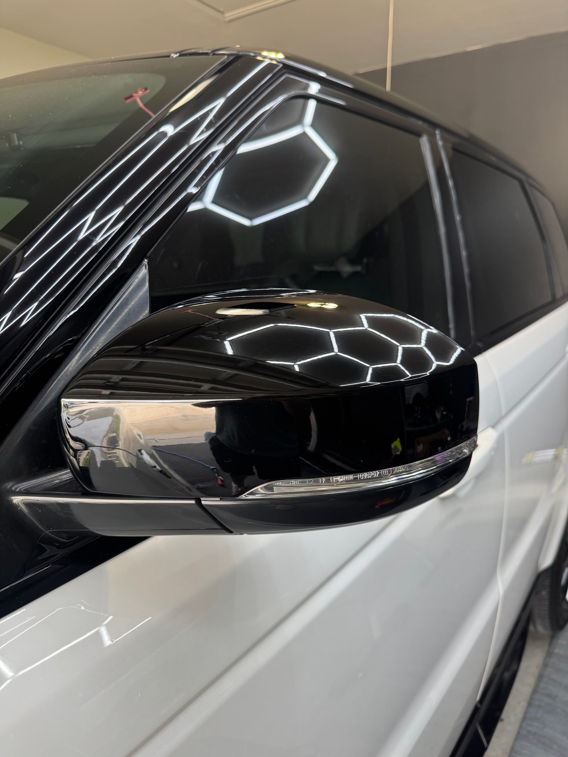 Close-up of a black car side mirror and tinted window on a white vehicle in a garage.