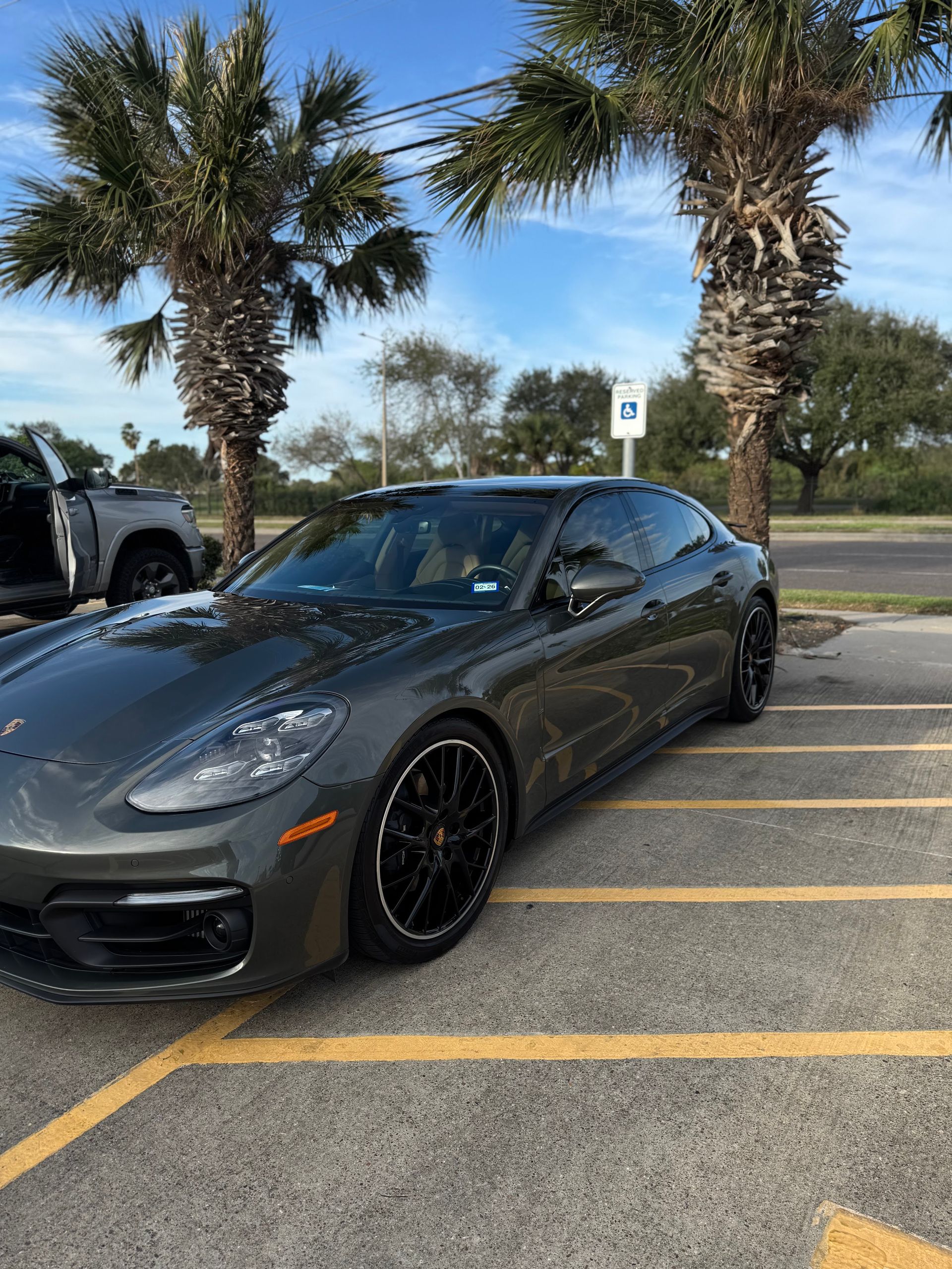 Dark gray sports car parked in a lot with palm trees and yellow lines nearby
