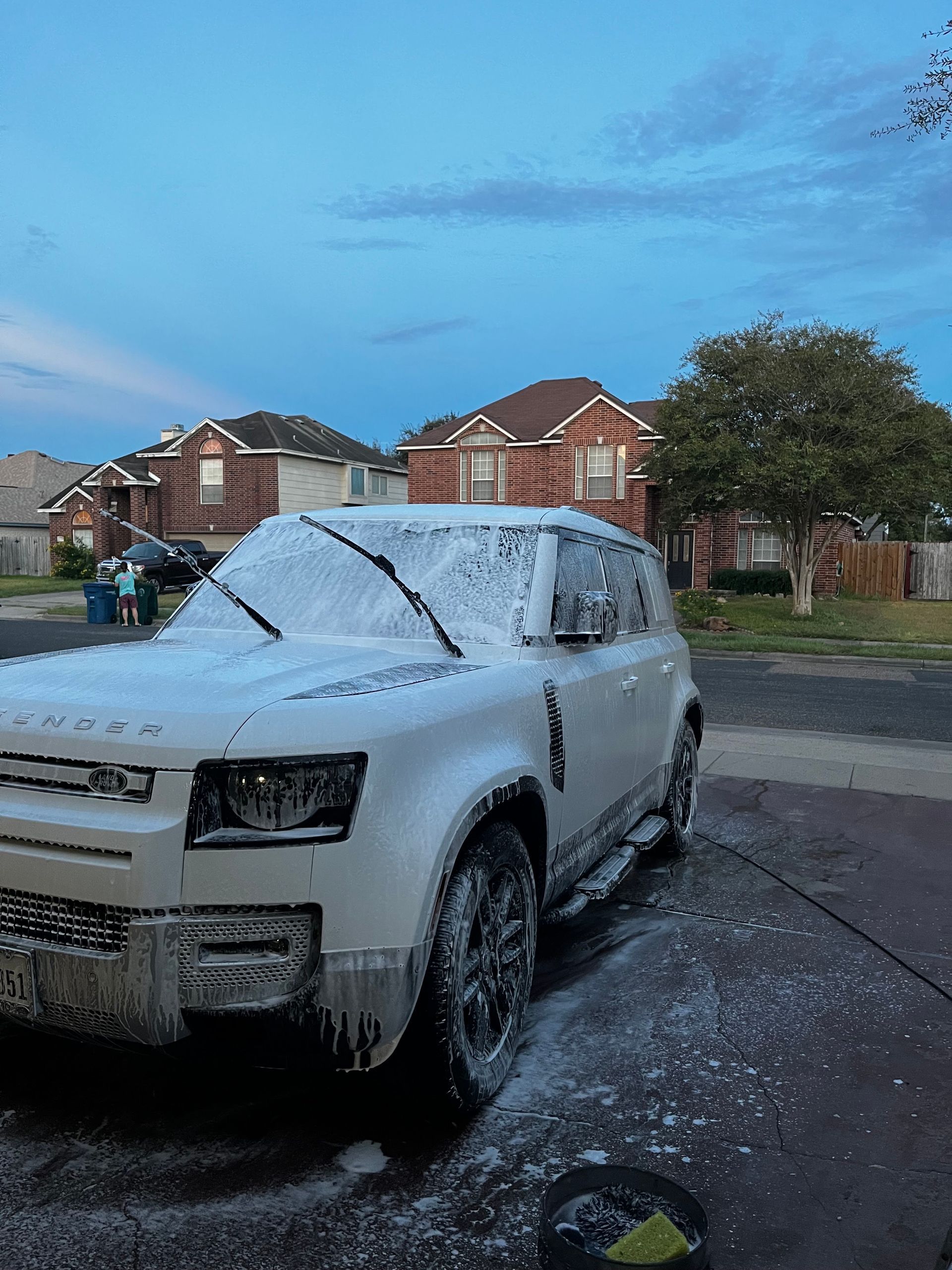 Snow-covered white SUV parked on a wet suburban street at dusk
