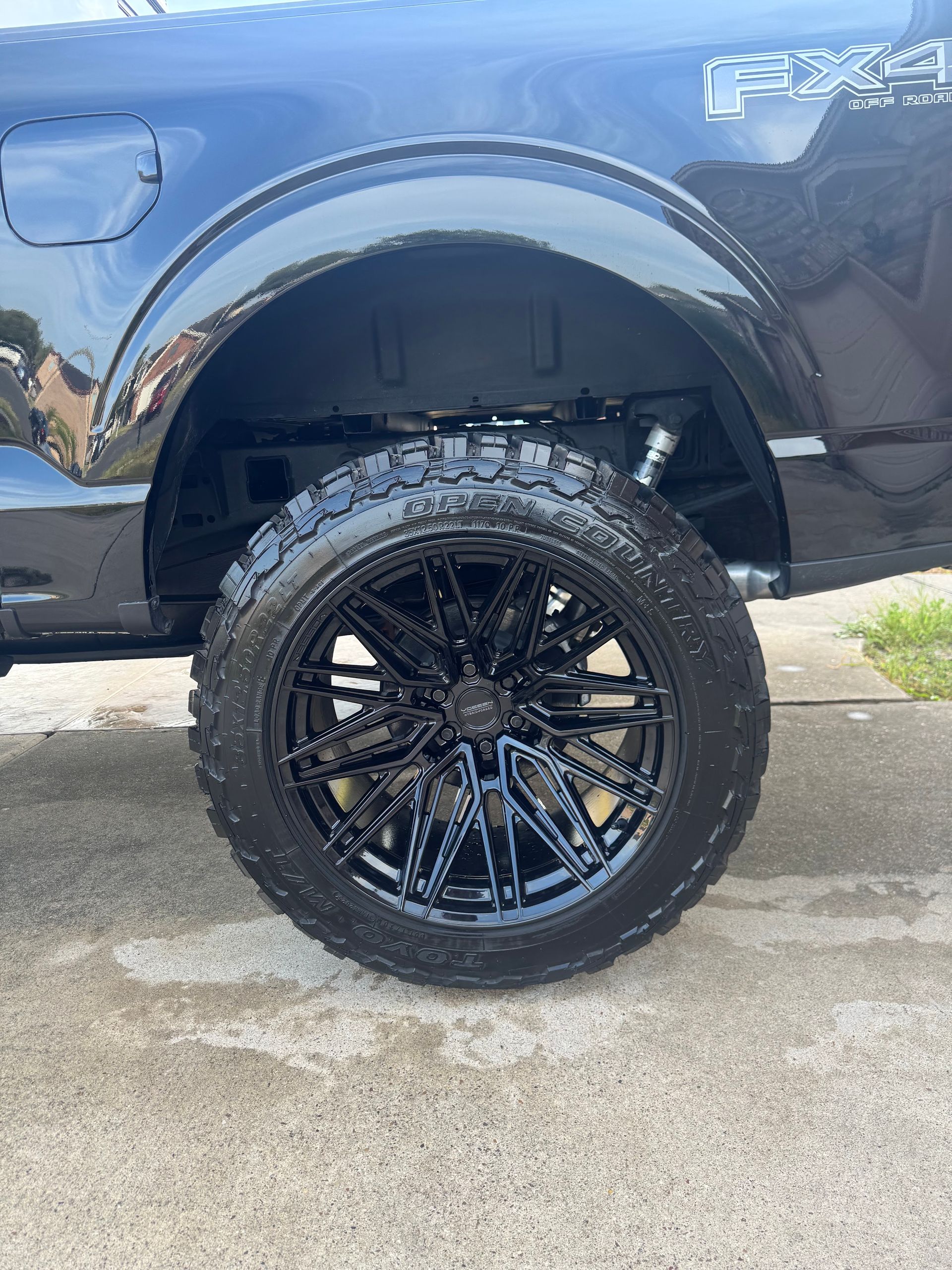 Blue pickup truck with oversized black custom wheel and tire parked on a wet driveway