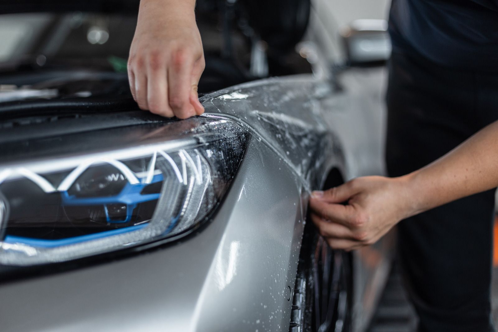 Person polishing a silver car headlight with a blue microfiber cloth and spray bottle