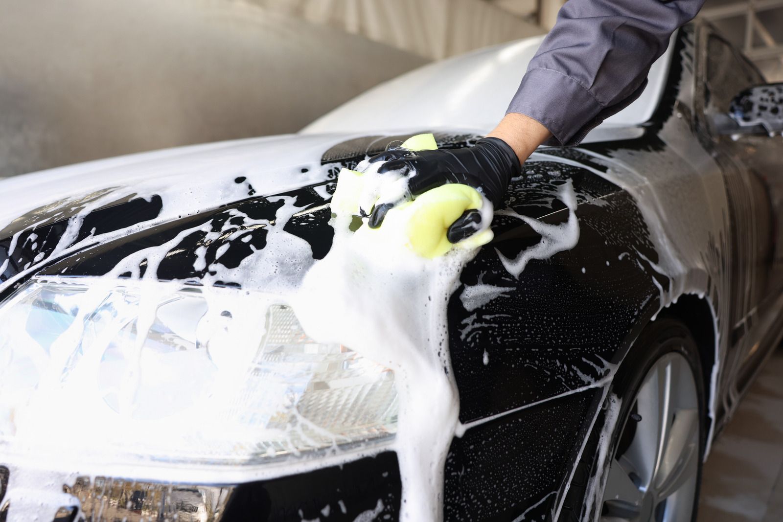Person washing a black car with soap foam in a driveway