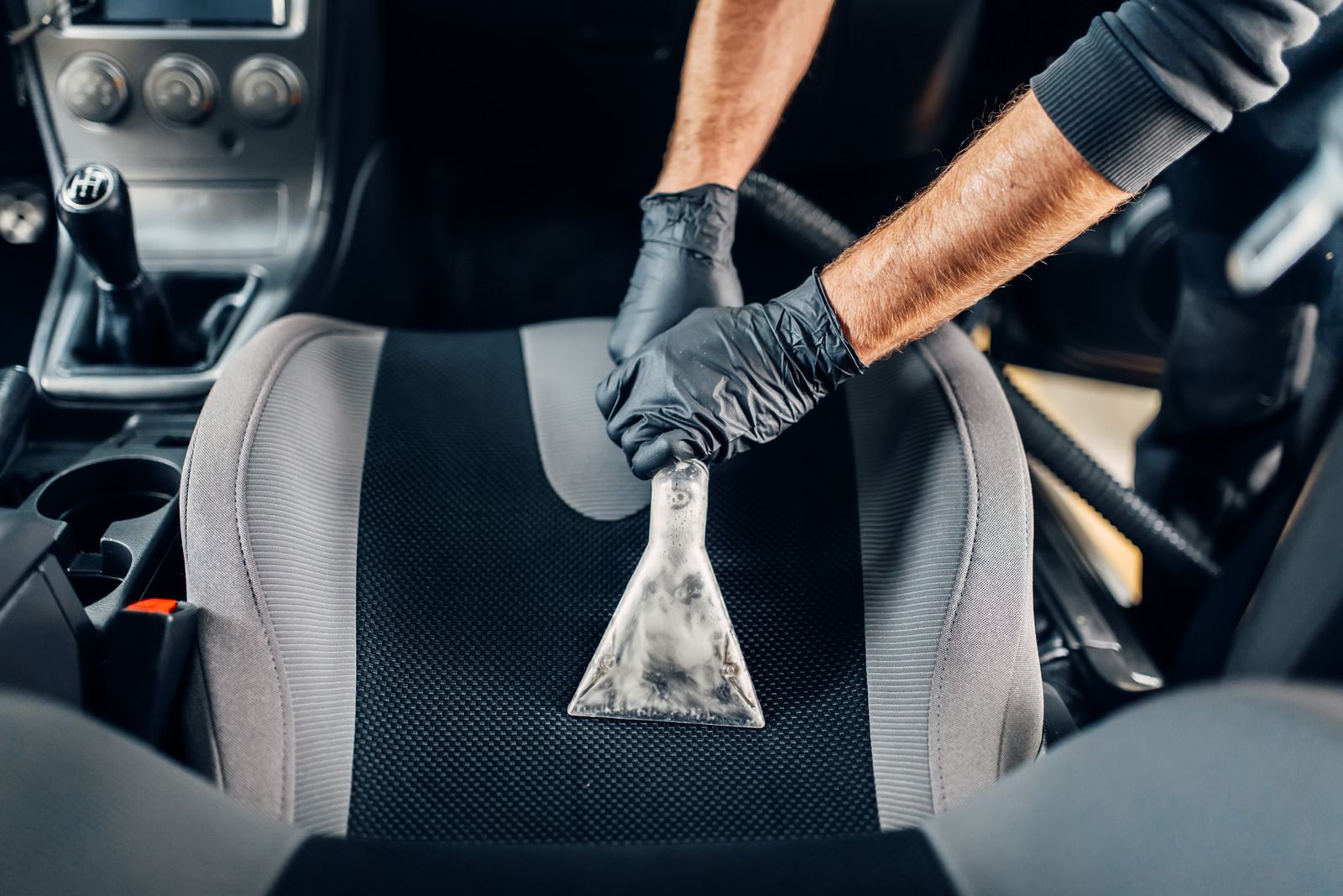 Person polishing a silver car headlight with a blue microfiber cloth and spray bottle