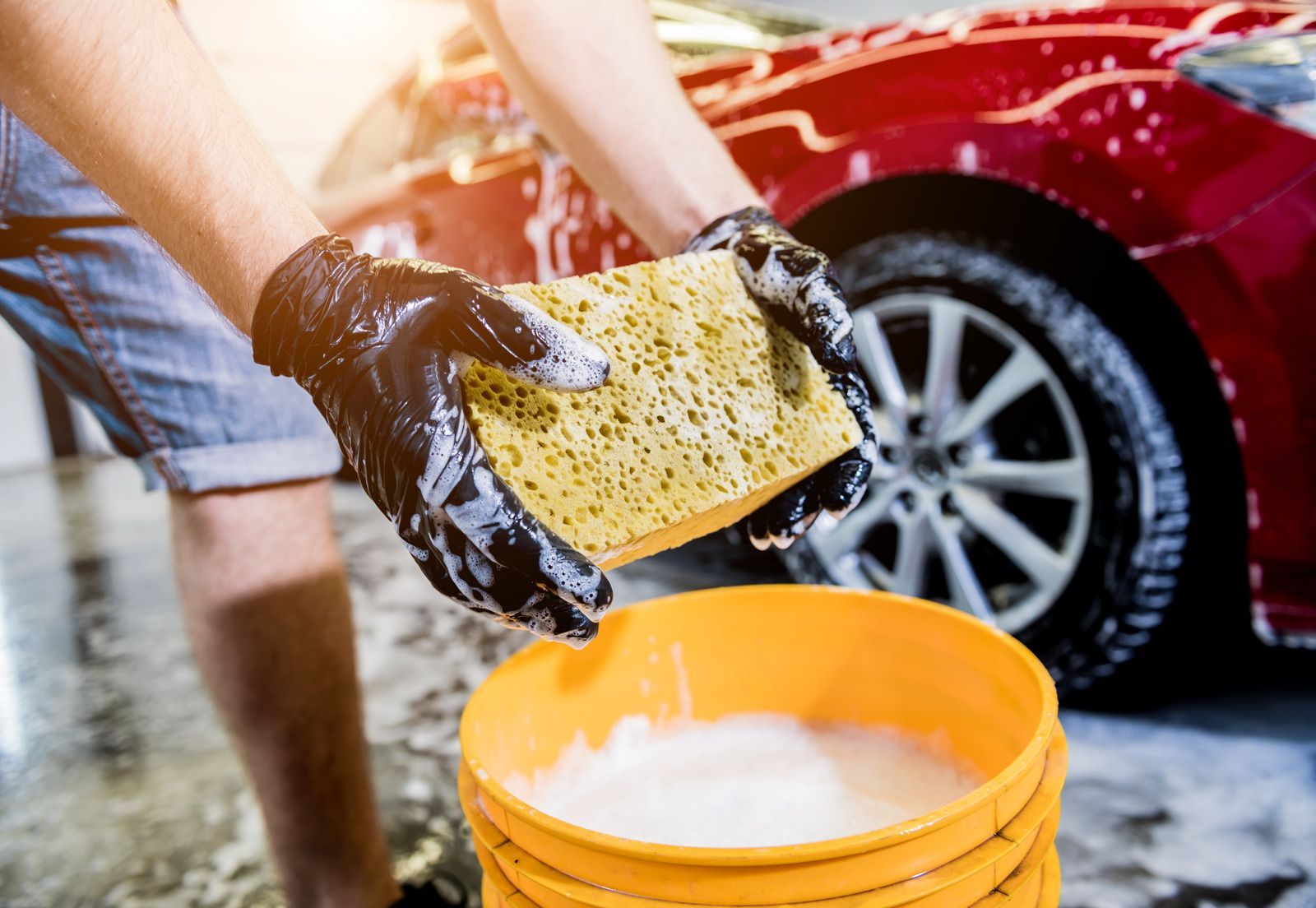 Person washing a black car with soap foam in a driveway