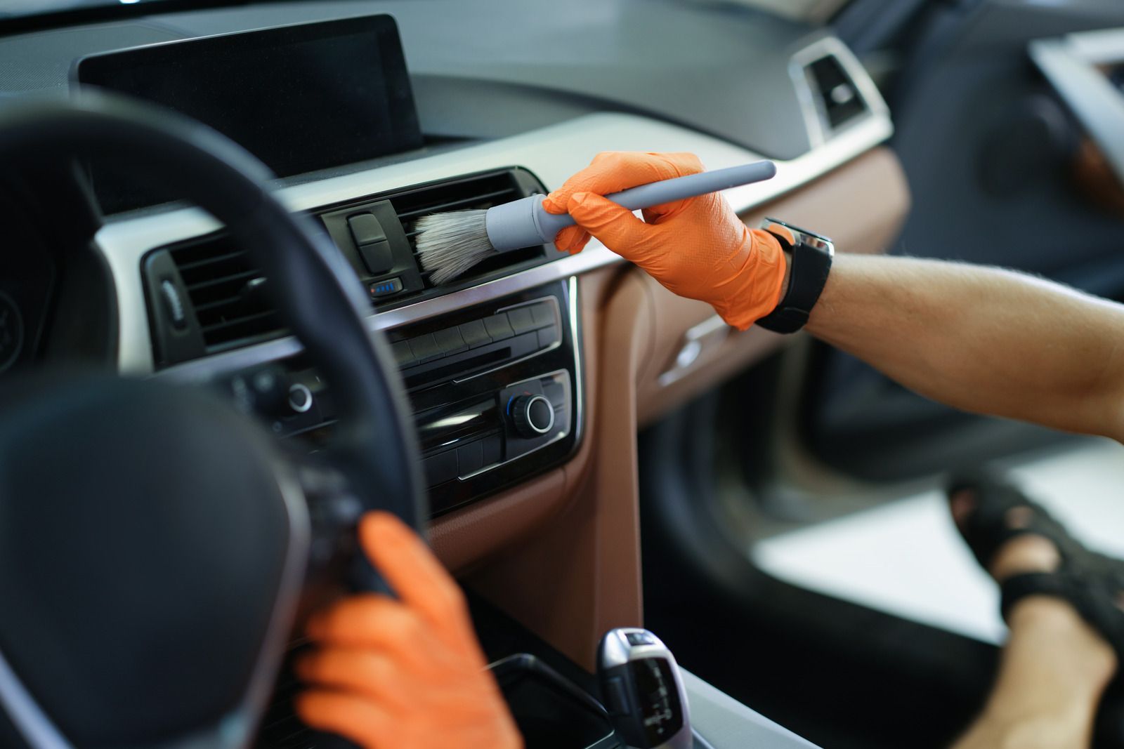 Person polishing a silver car headlight with a blue microfiber cloth and spray bottle