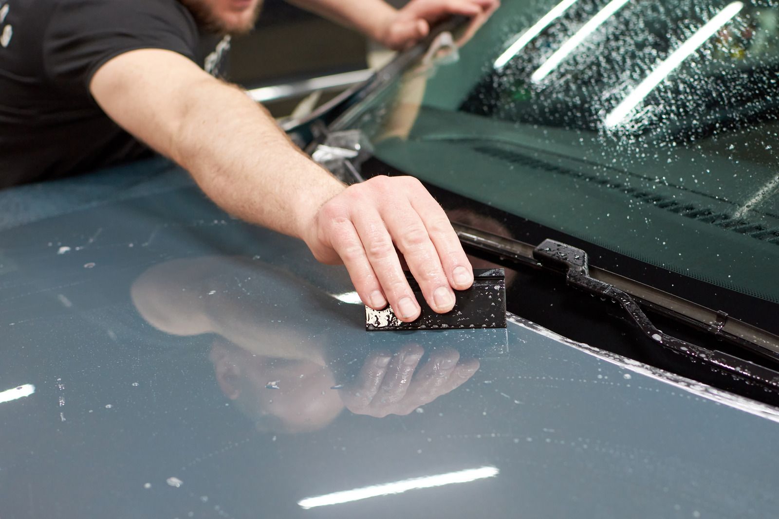 Person washing a black car with soap foam in a driveway