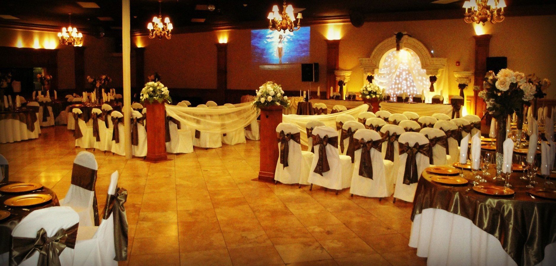 Elegant banquet hall with white-draped tables, floral centerpieces, and warm ambient lighting