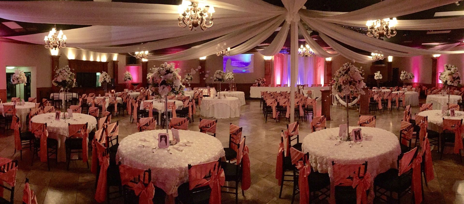 Decorated banquet hall with round tables, red chairs, and draped ceiling lighting for an event