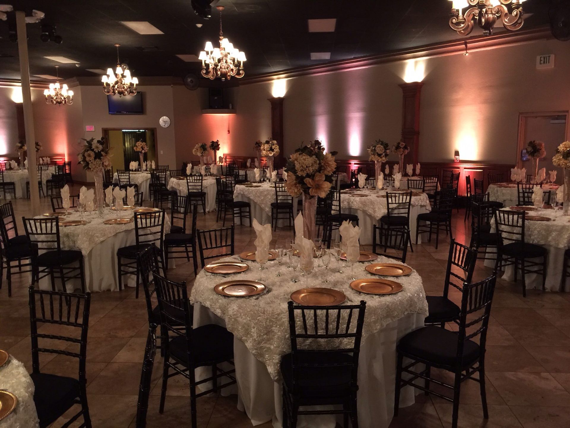 Banquet hall with round tables, black chairs, and floral centerpieces under warm chandelier lighting