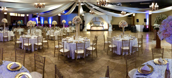 Elegant white tiered cake display on a silver table with small matching cakes and floral decor in front of draped curtains