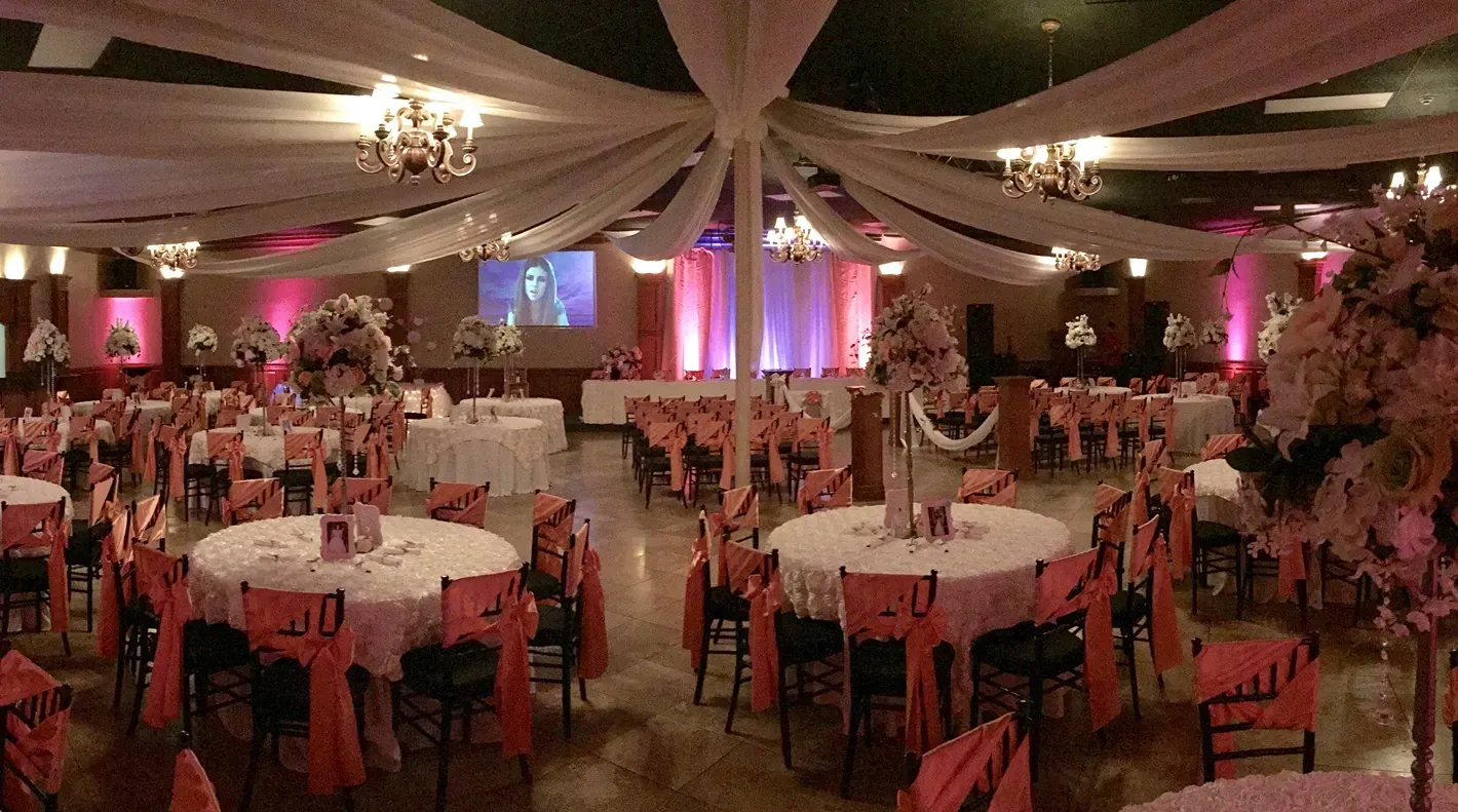 Decorated banquet hall with round tables, pink lighting, and draped ceiling fabric for an event