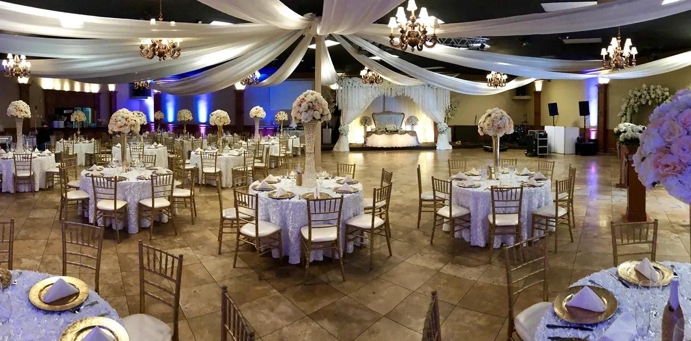 Elegant banquet hall with round tables, white drapes, floral centerpieces, and soft blue lighting
