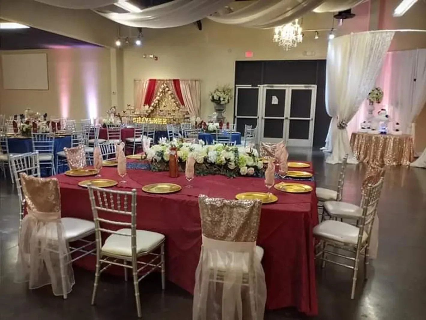 Decorated banquet hall with round tables, maroon tablecloths, and white drapes for an event