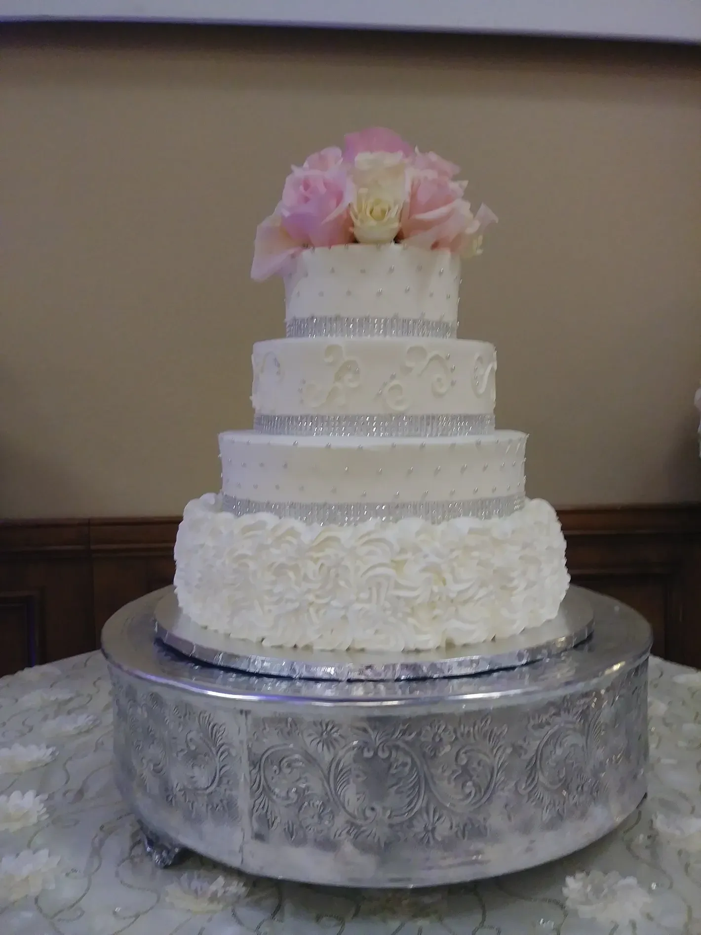 Five-tier white wedding cake with pink flowers on a silver stand