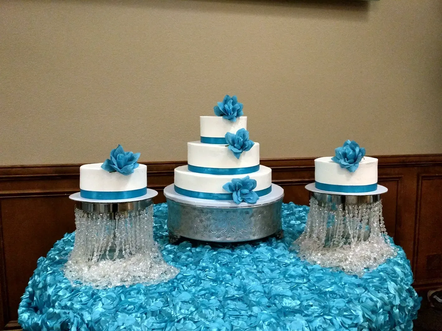 Blue and white tiered display on a blue tablecloth, with matching floral accents and silver draped stands