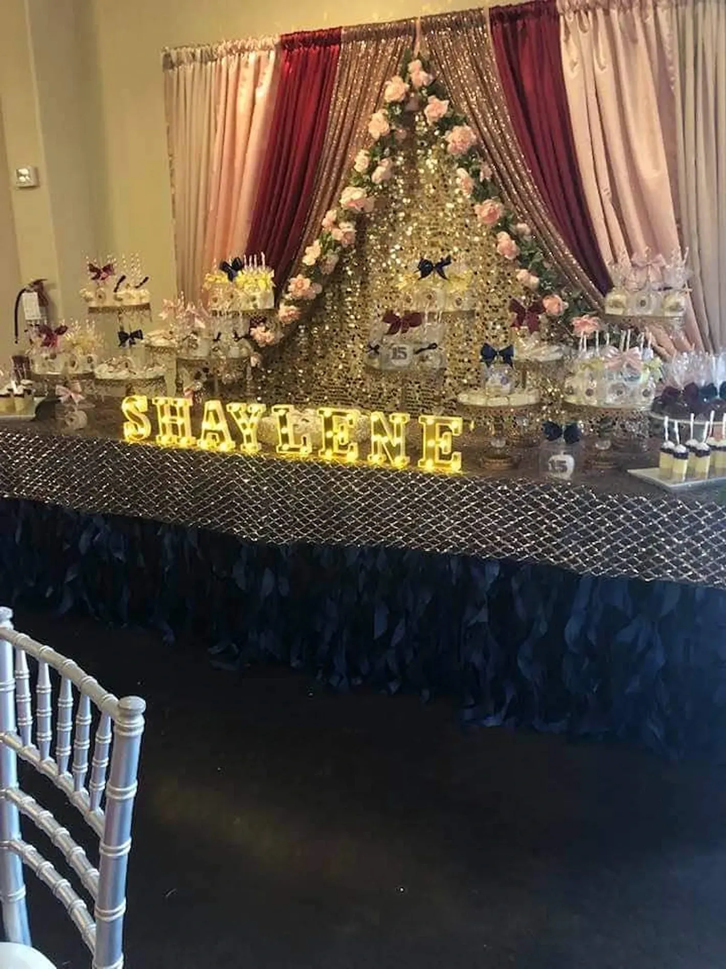 Decorated banquet table with flower backdrop, gold letters, and draped curtains for a celebration