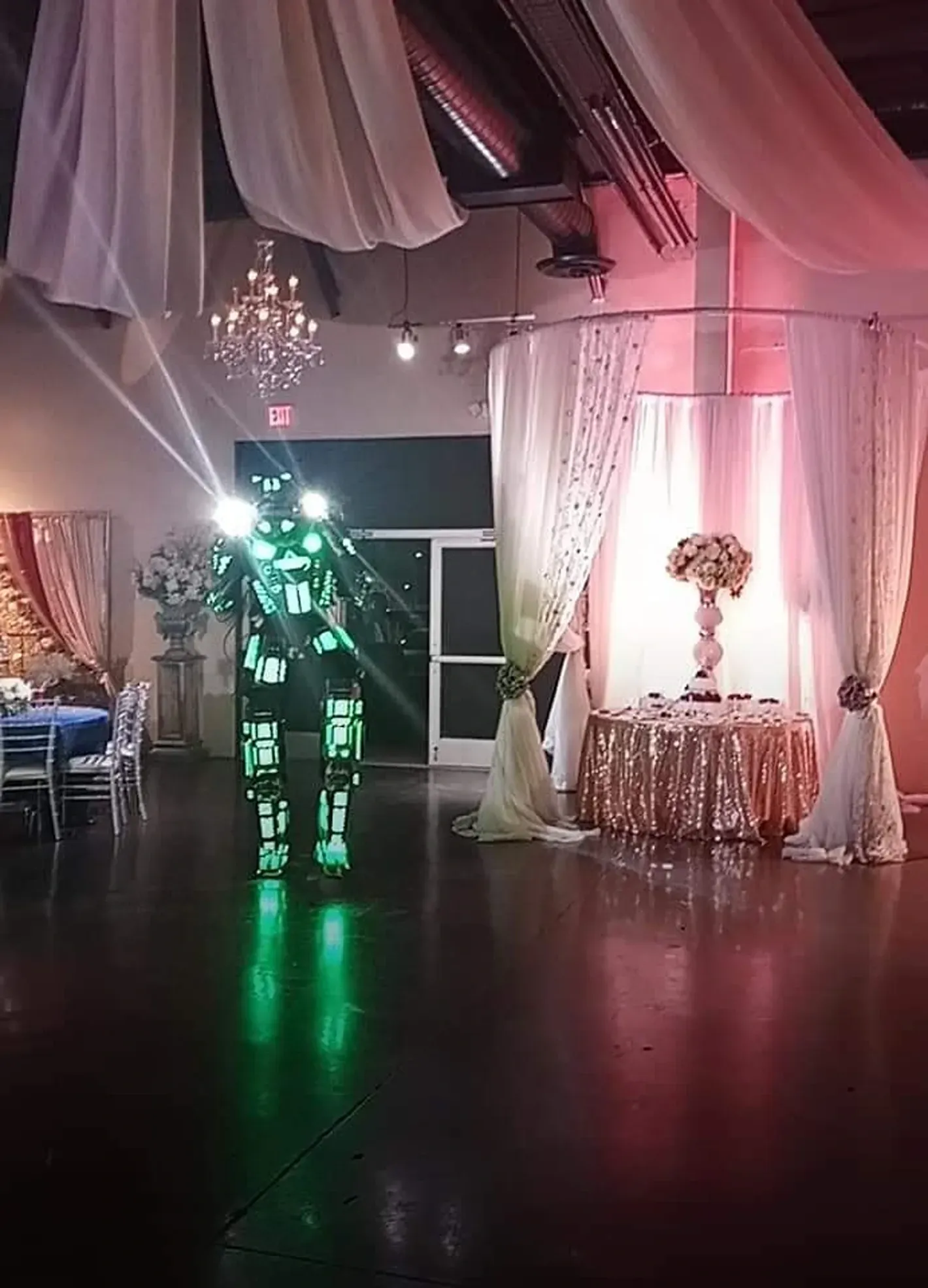 Person in illuminated robotic suit on a decorated dance floor with draped ceiling and glowing green light