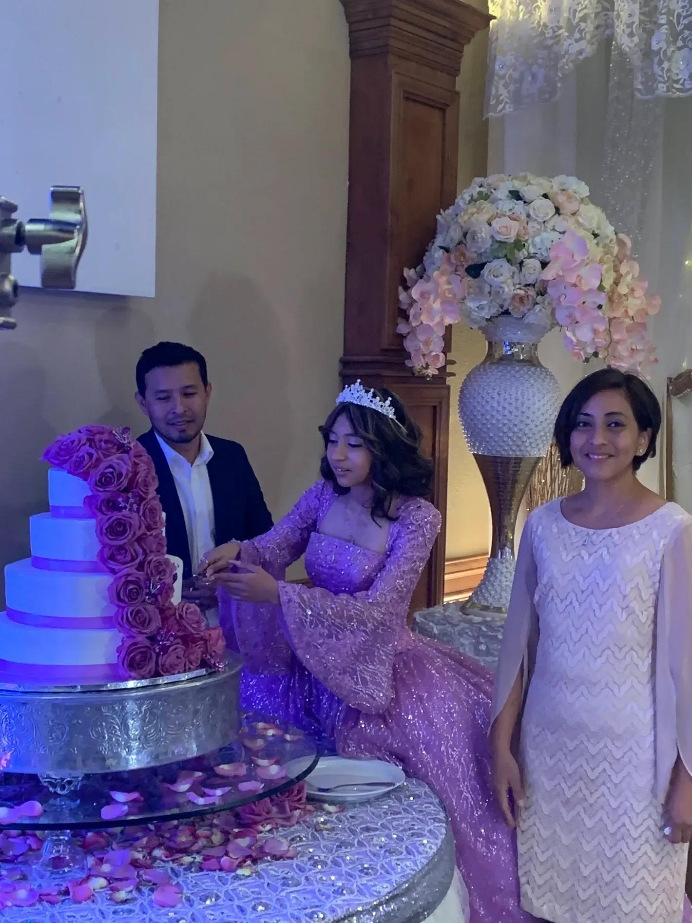 Two people and a child beside a pink cake at a decorated celebration table