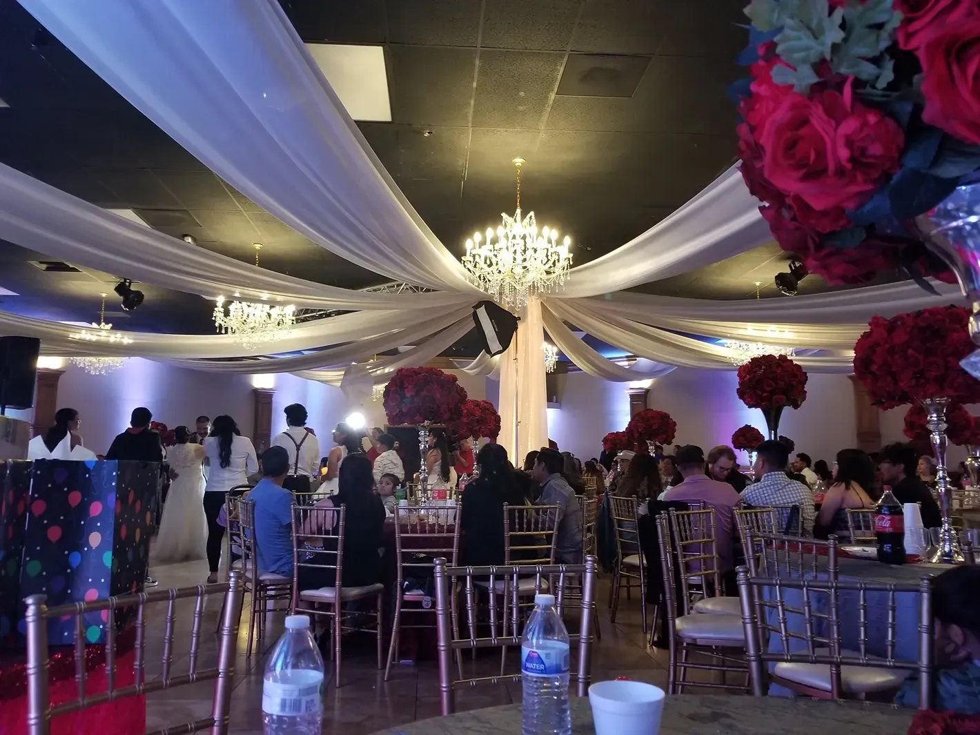 Elegant banquet hall with draped ceiling, chandelier, and guests seated at tables under pink floral decor