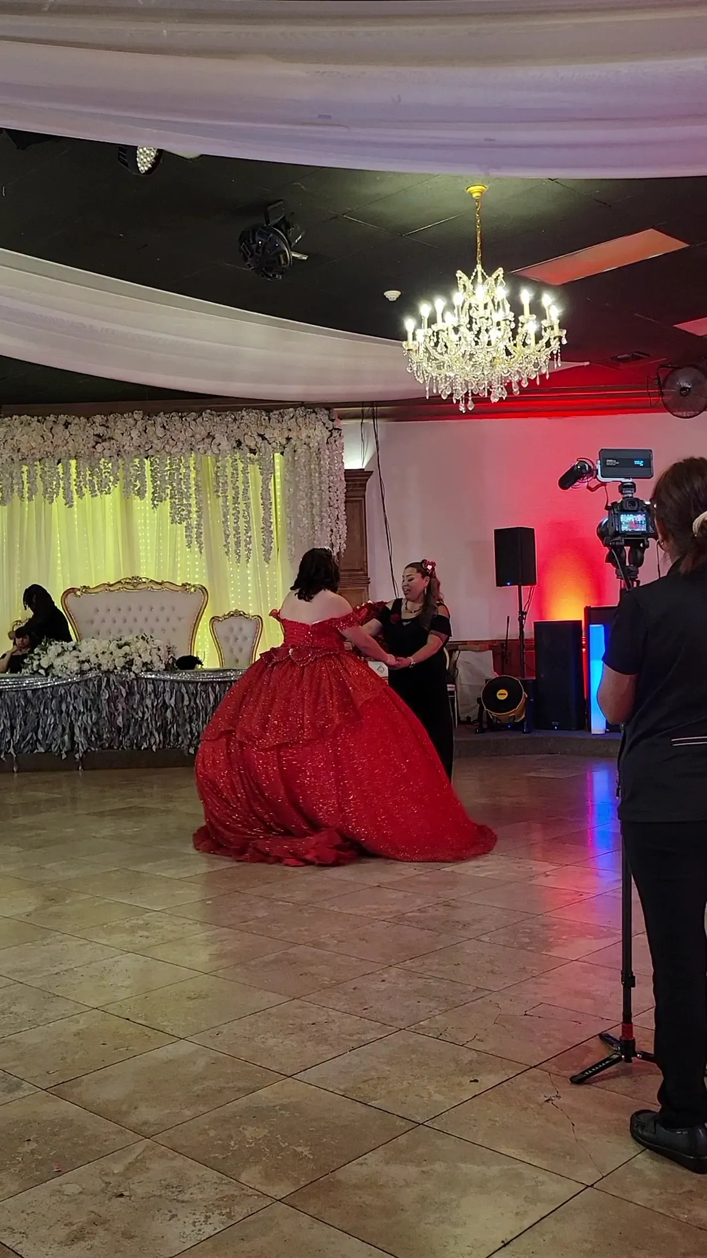 Woman in a red gown dancing in a decorated banquet hall with chandeliers and draped ceiling.