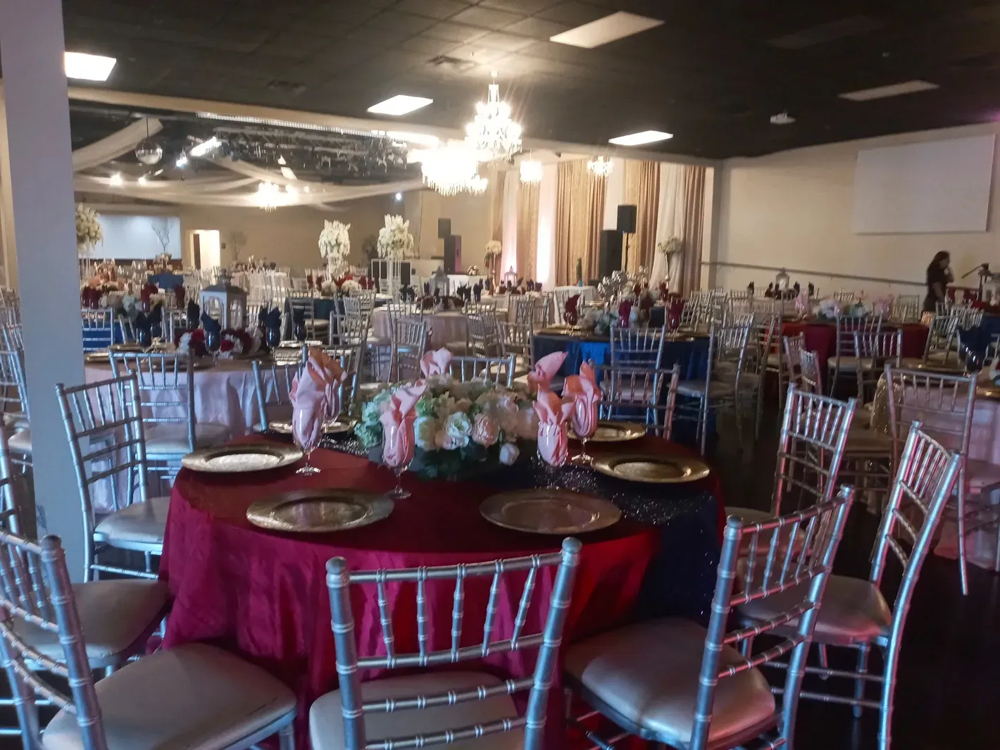 Banquet hall with round tables set for a formal event, featuring burgundy tablecloths and silver chairs