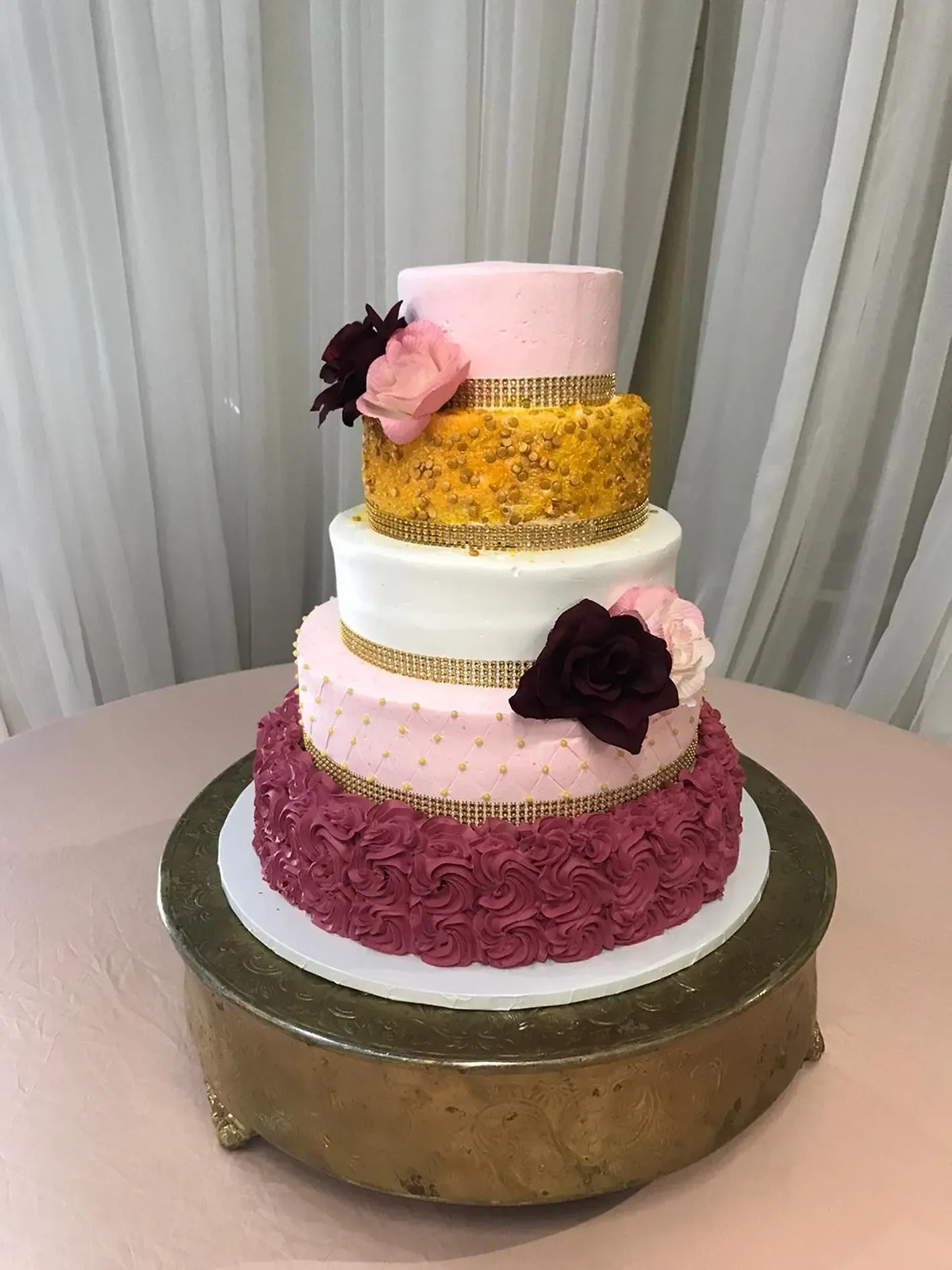 Four-tier pastel cake with pink, yellow, and burgundy ruffles on a gold cake stand