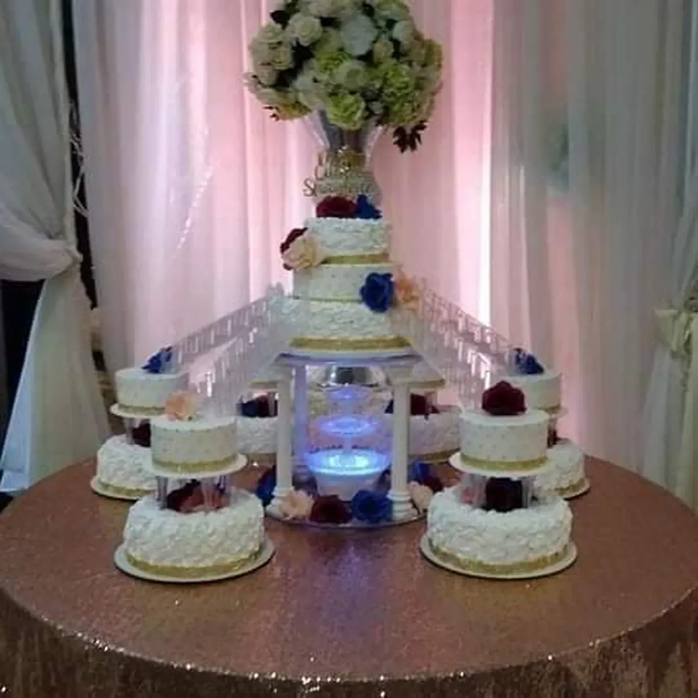 Elegant tiered wedding cake display with white cakes, blue accents, and floral topper on a round table