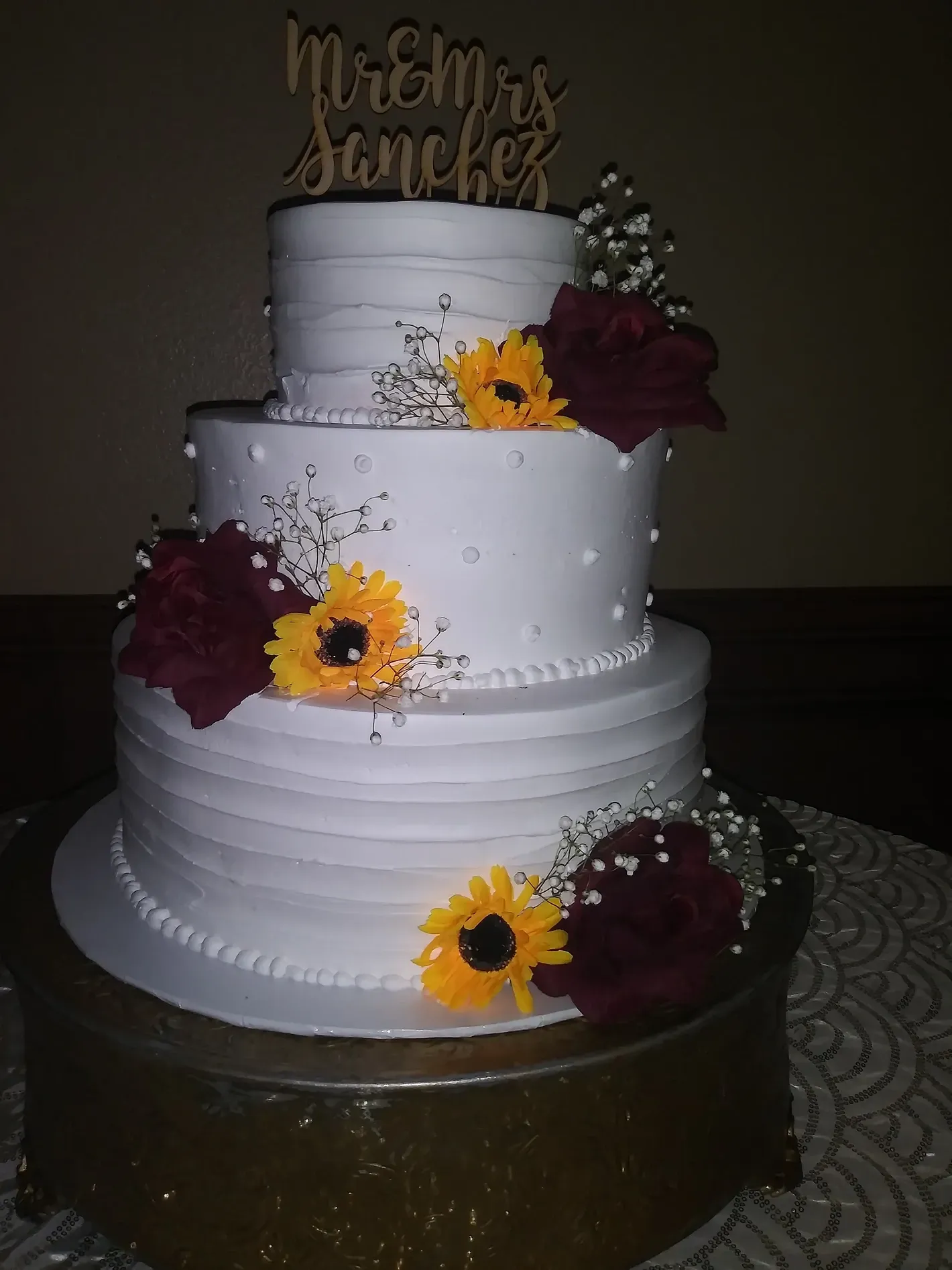 Three-tier white wedding cake with yellow and burgundy flowers and a gold topper