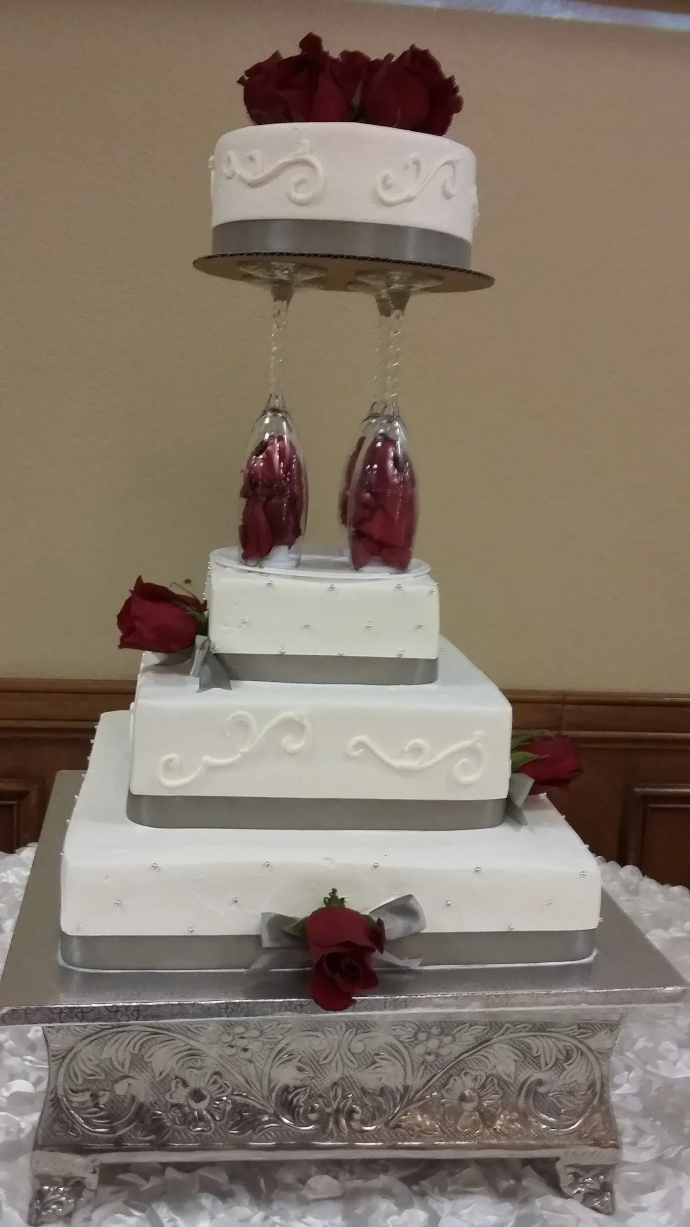 Tiered white wedding cake with red roses and silver decorations on a table
