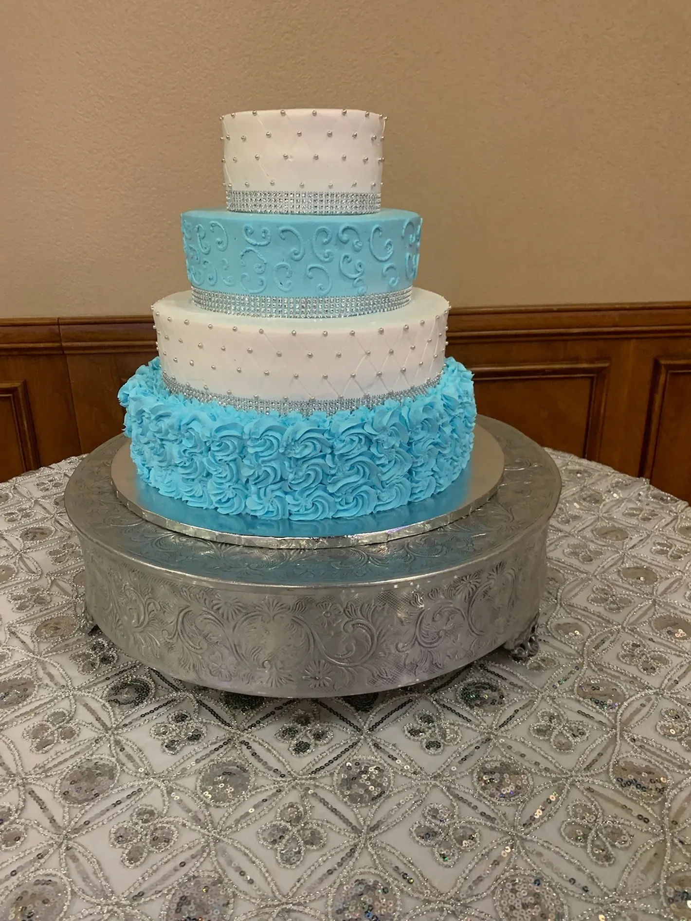 Four-tier white and blue rosette cake on a silver pedestal table