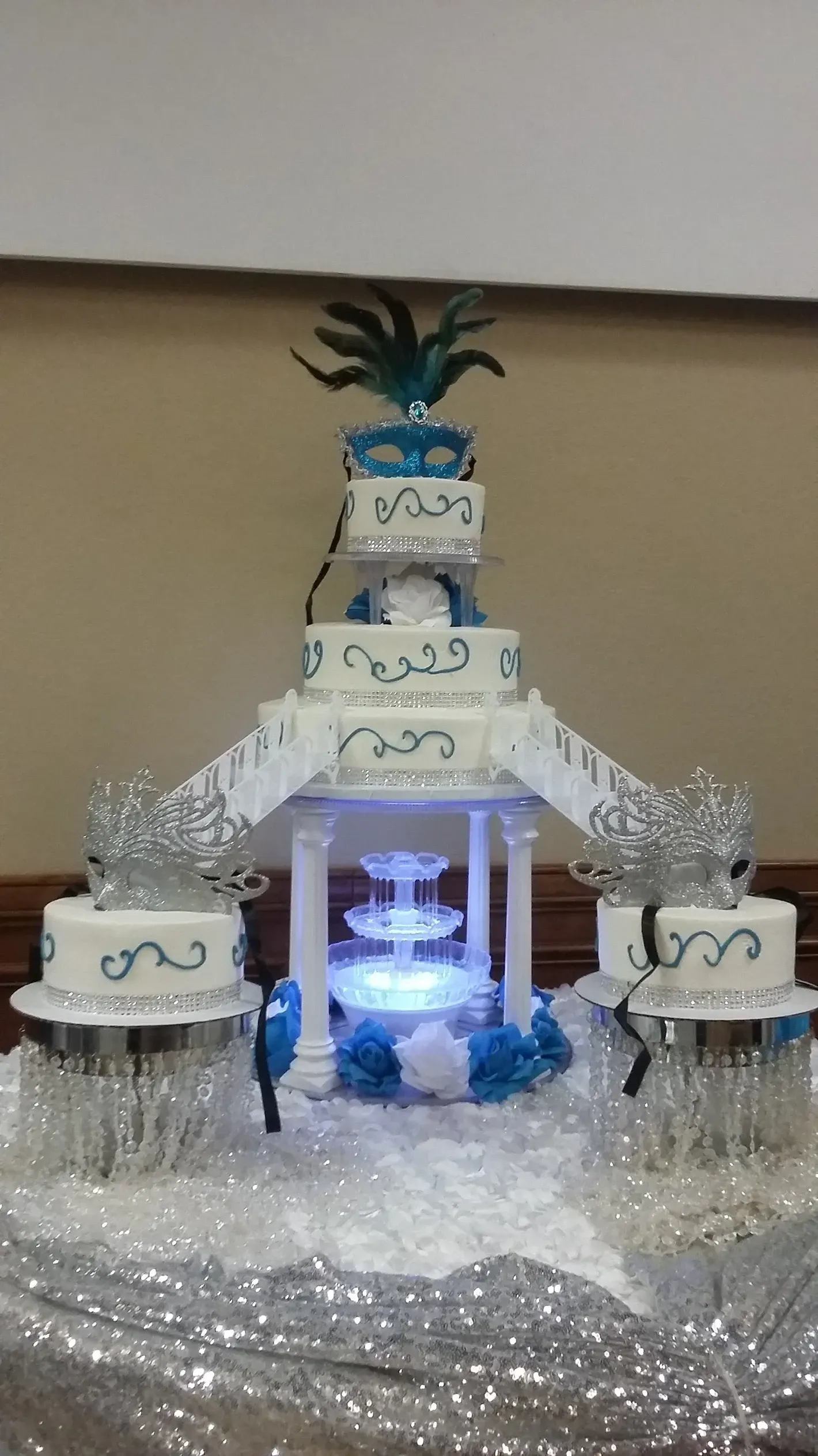 White tiered decorative fountain with blue lights and silver tinsel on a table