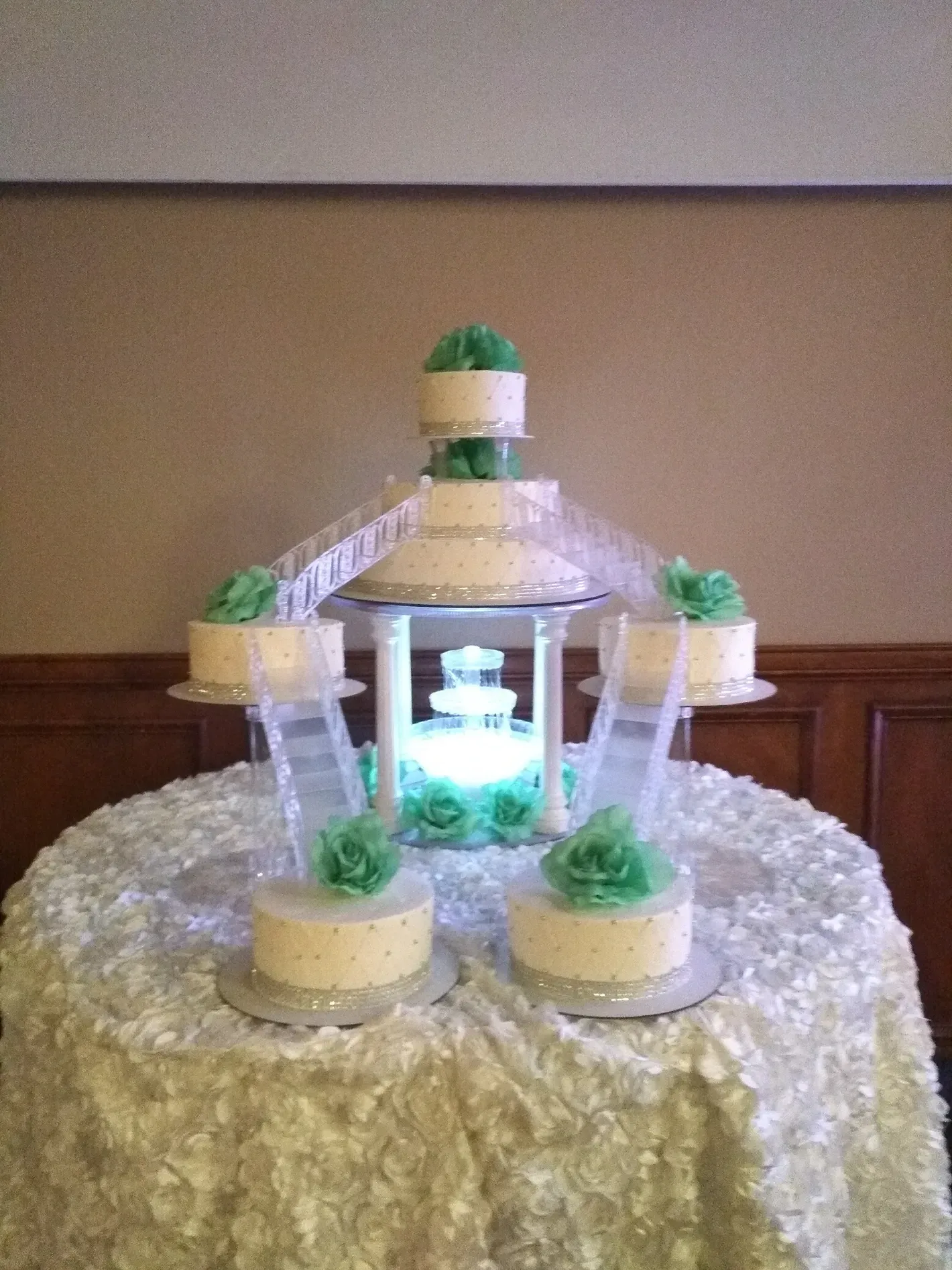 Decorative illuminated bottle fountain with green plants on a draped table centerpiece