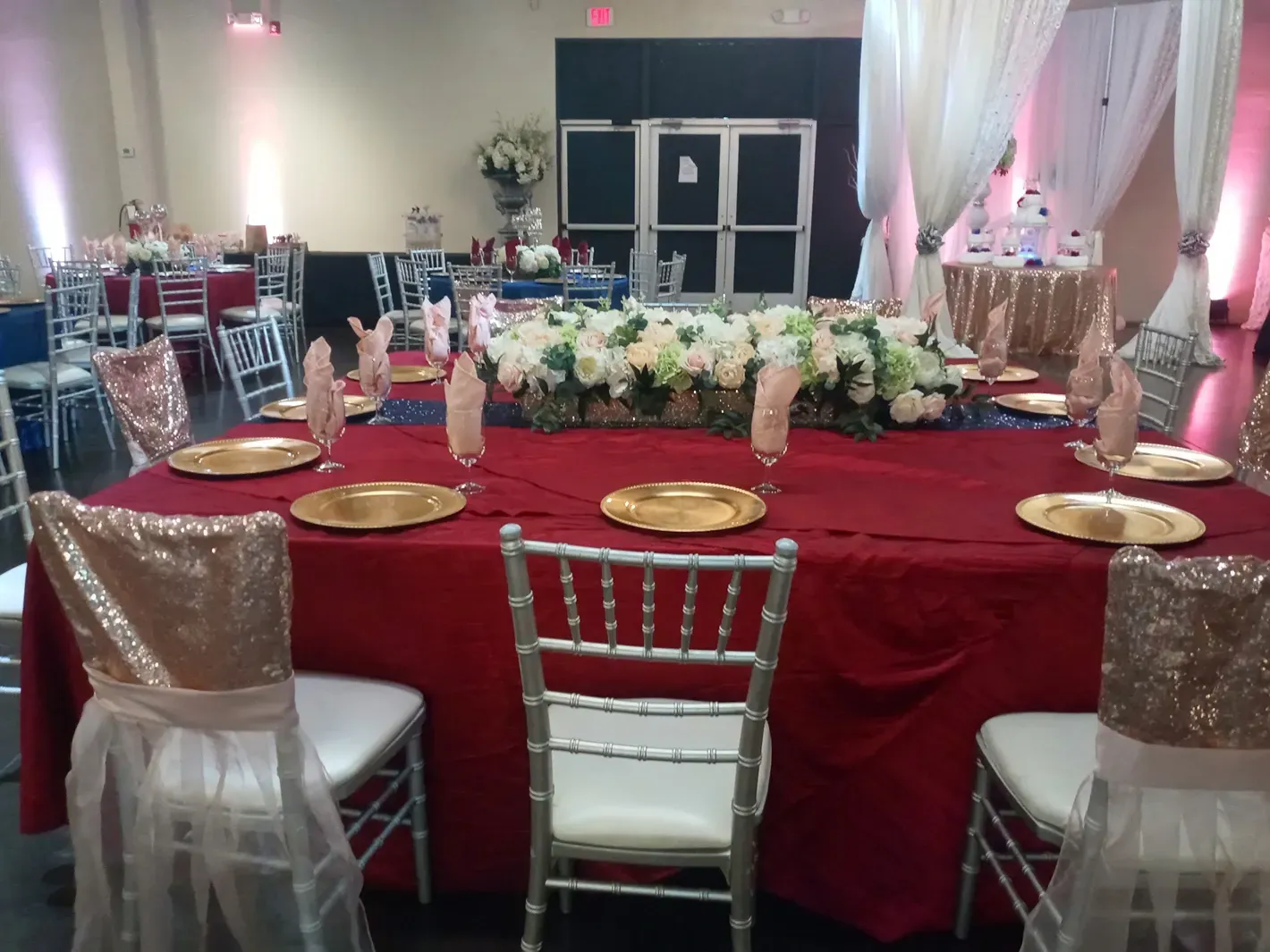 Elegant banquet table with red tablecloth, gold plates, and floral centerpiece in a decorated event hall