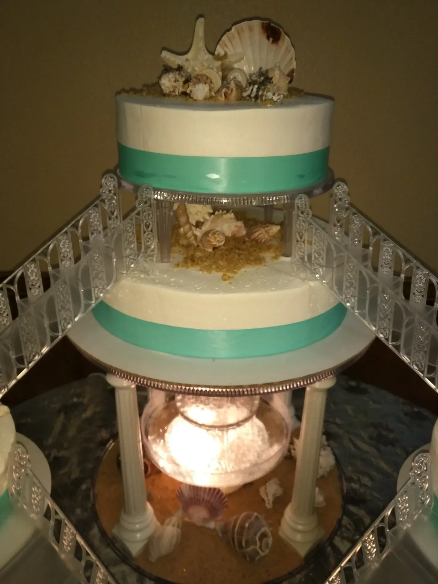 Decorated multi-tier cake with turquoise ribbon and cat figurine topper on a mirrored stand