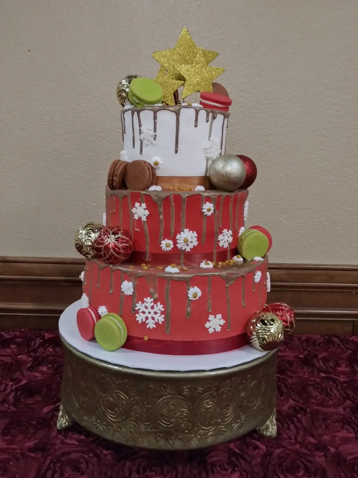 Three-tier decorated cake with red and white frosting, gold accents, and candy decorations on a stand
