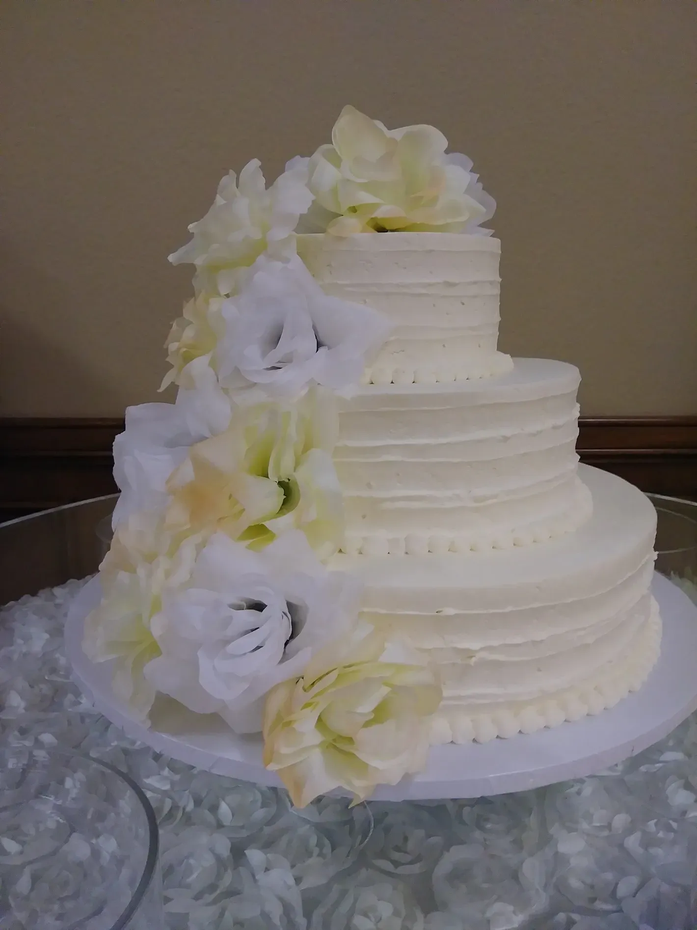 White two-tier wedding cake with cascading white and pale yellow flowers on a table