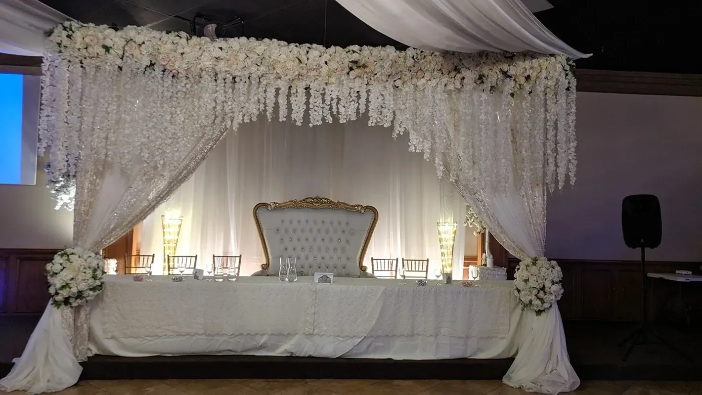 Elegant wedding stage with white draped canopy, floral decorations, and ornate chairs on a decorated platform