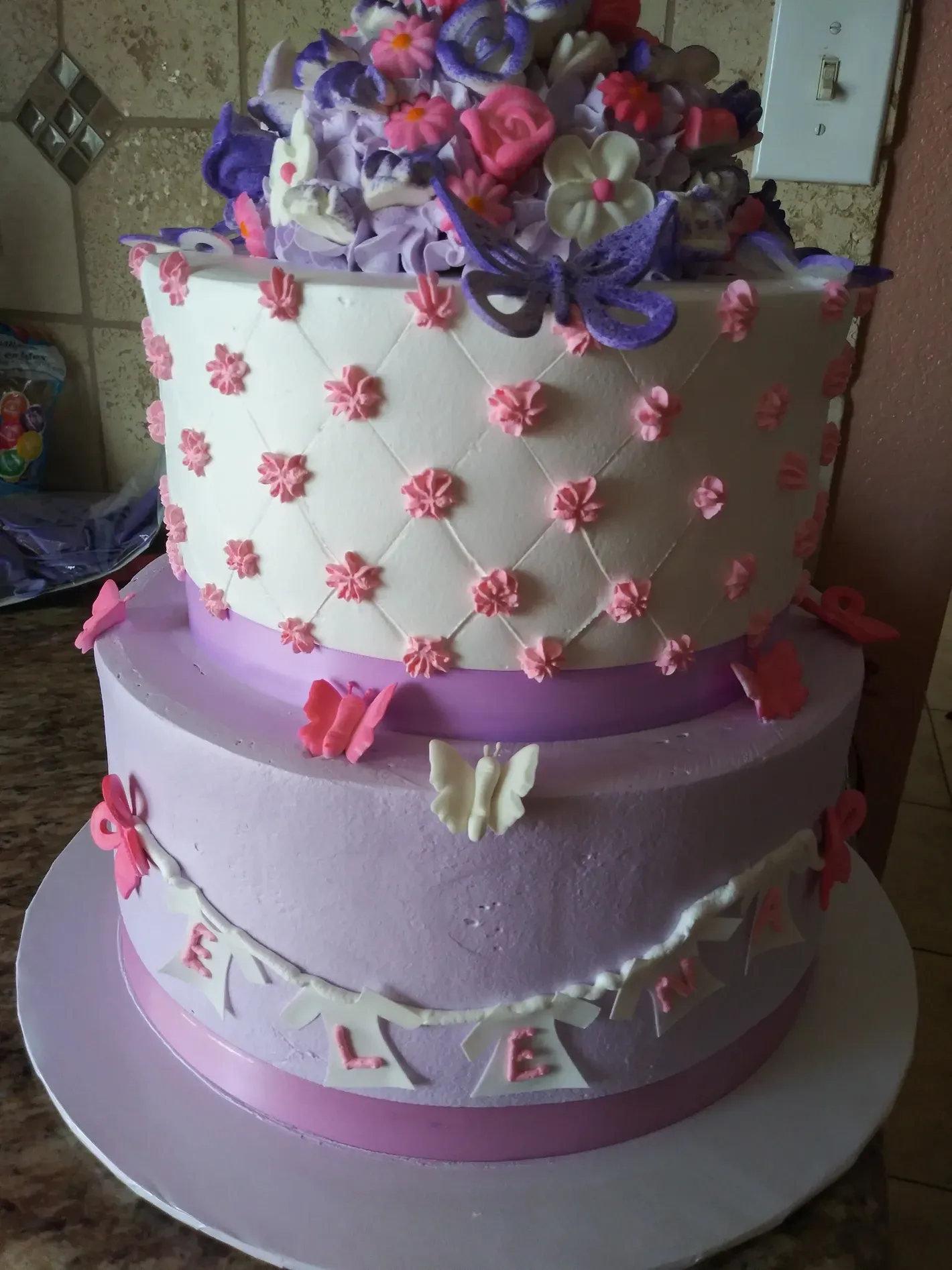 Two-tier decorated cake with pink and purple frosting and ribbon accents