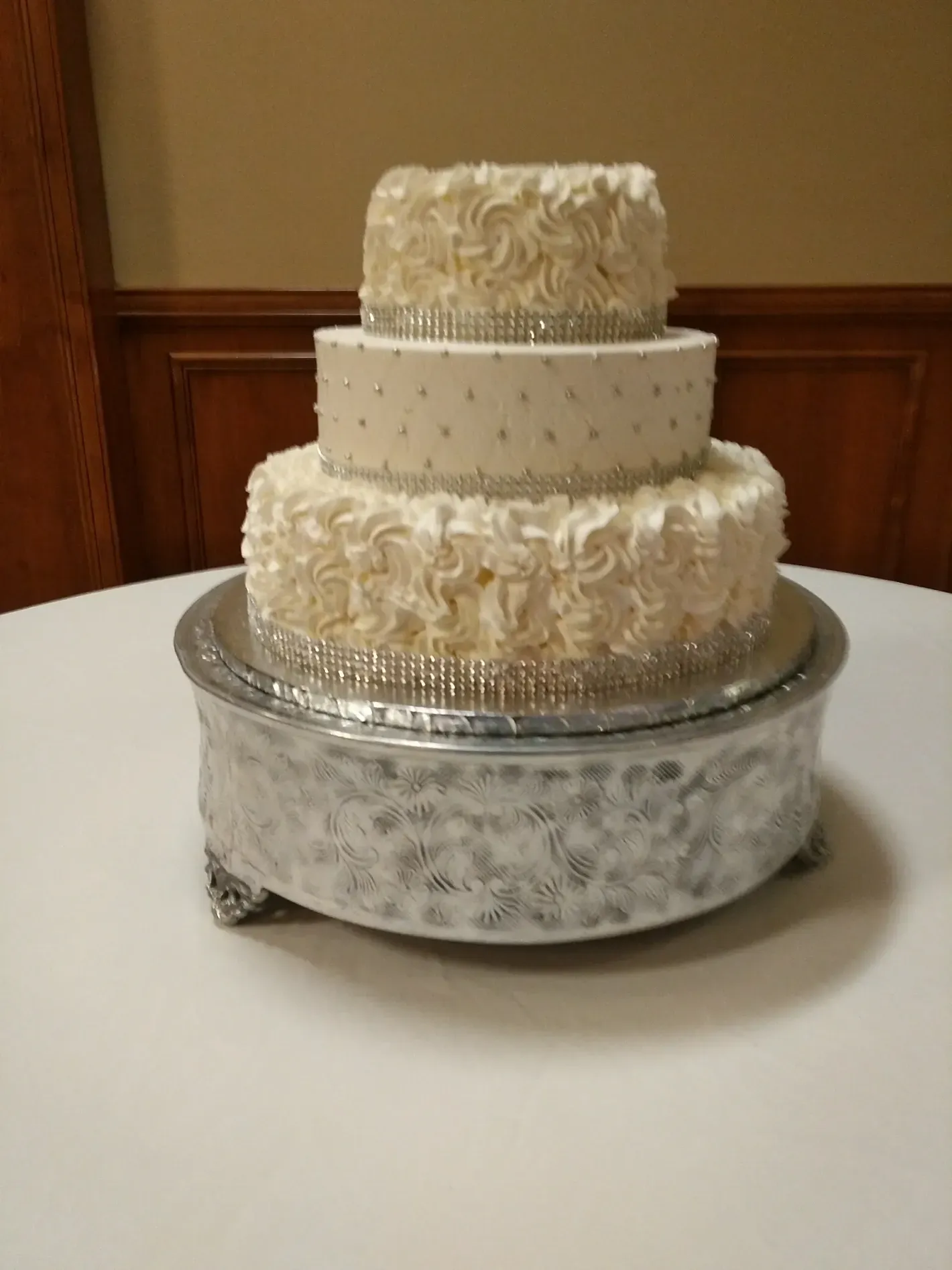 Three-tier white frosted cake on a decorative silver stand in a banquet room