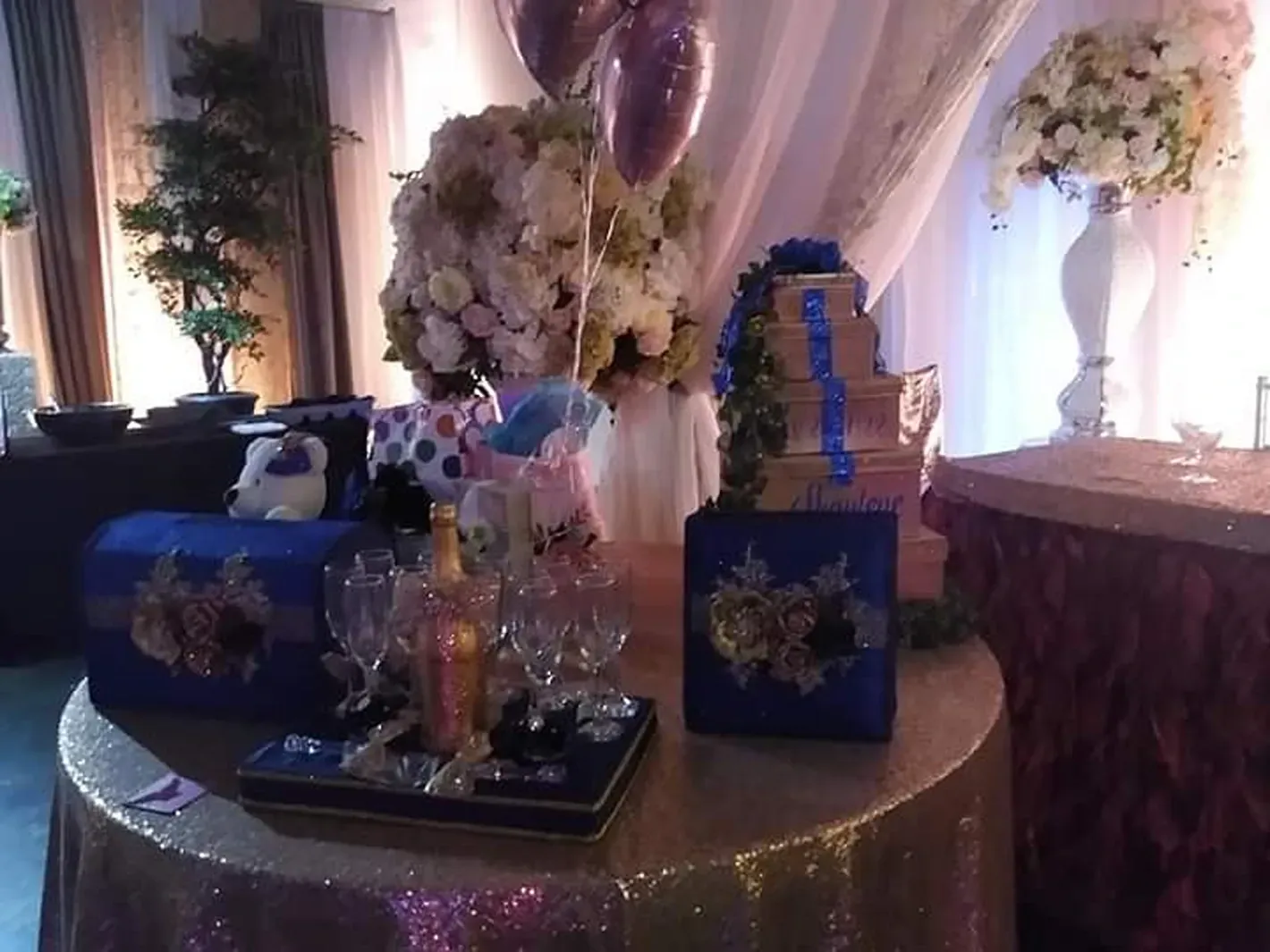 Decorated party dessert table with blue gift boxes, cupcakes, champagne flutes, and floral arrangements