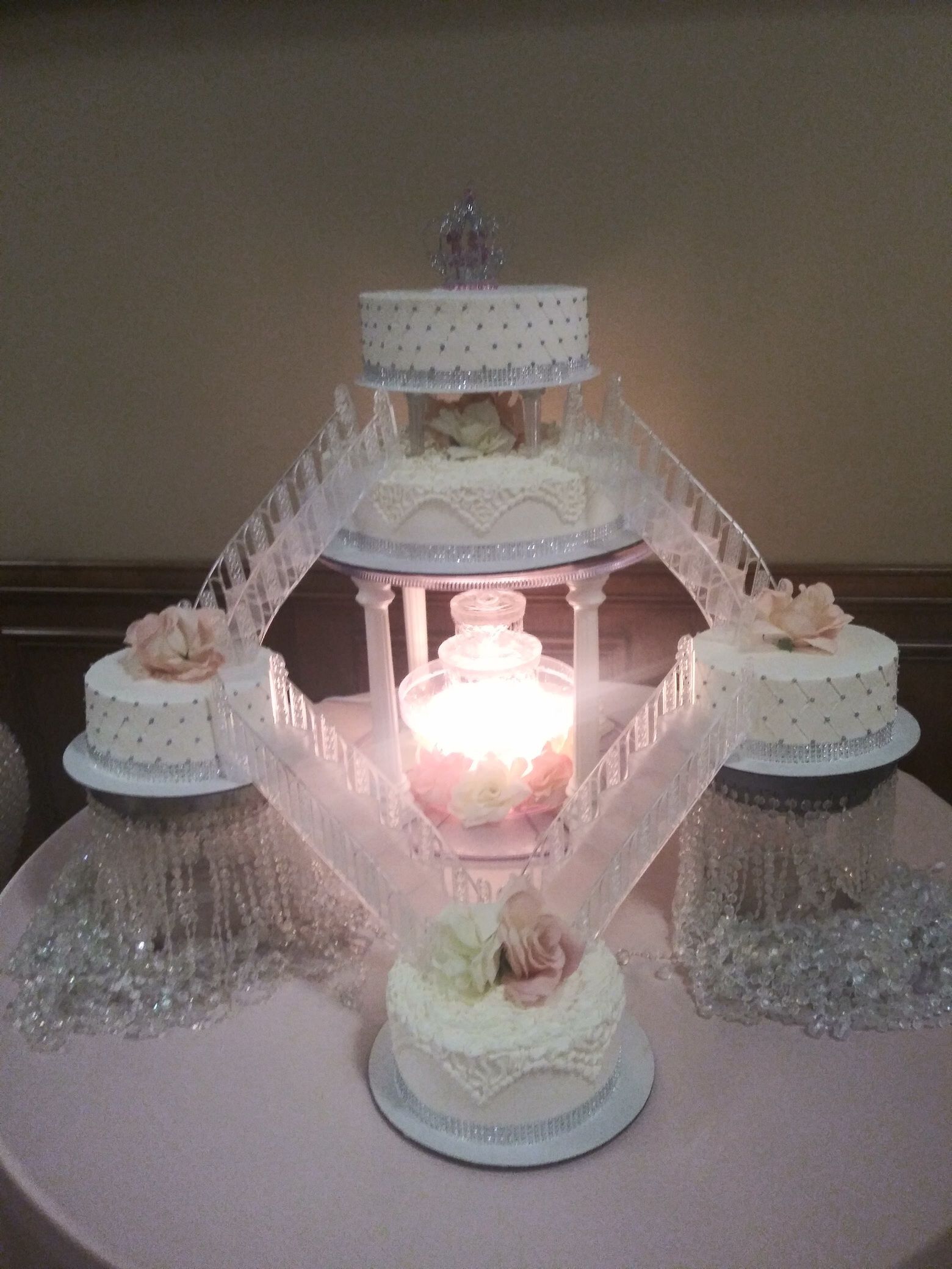 Pink tiered wedding cake with white lace ribbons and lit candle centerpiece