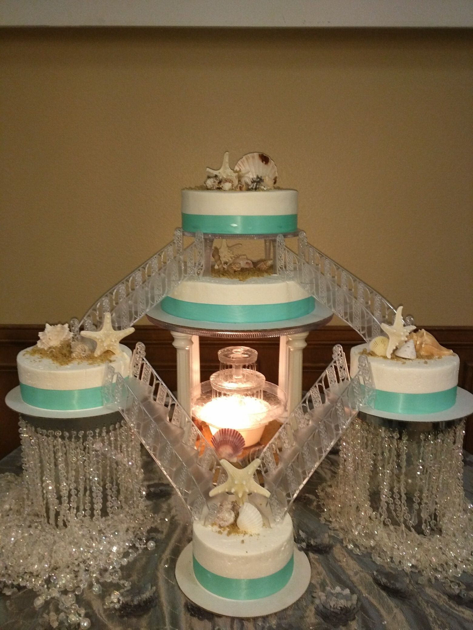 Decorative tiered fountain with white and teal tiers, sparkling water streams, and a glowing center flame.