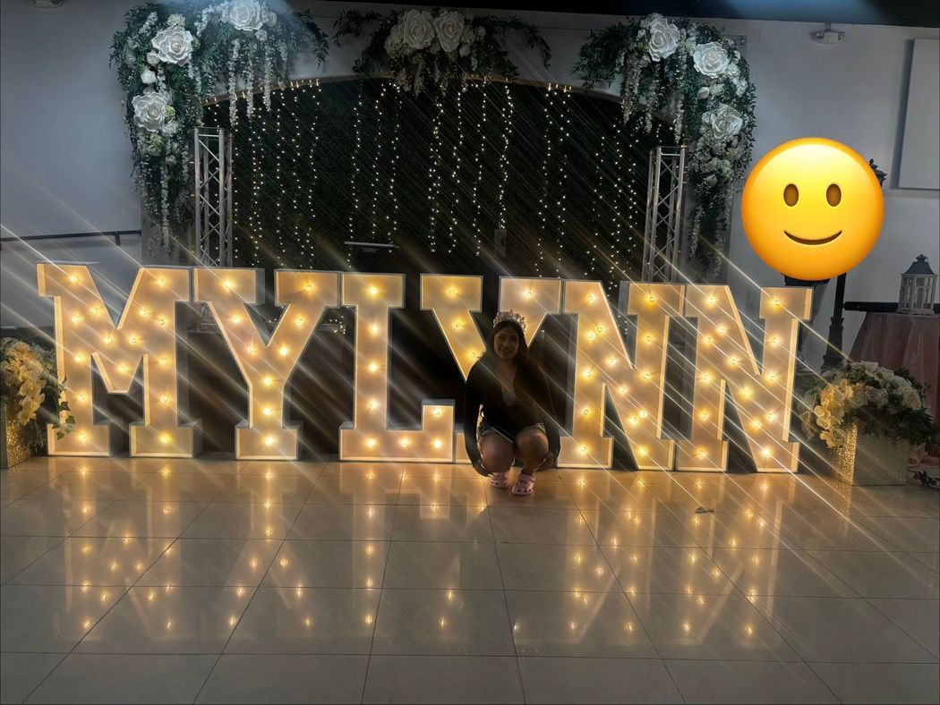 Illuminated “MYLYNN” marquee letters with a smiley balloon in a decorated indoor event space