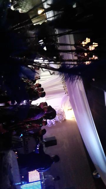 Indoor event venue with seated audience facing a bright stage under purple and white drapery