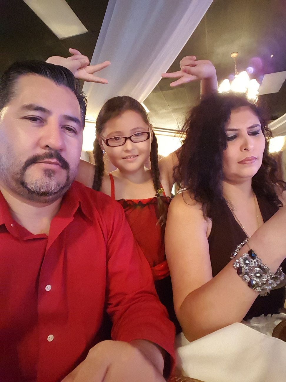 Three people seated at a table, with two posing playfully and one looking at a phone.