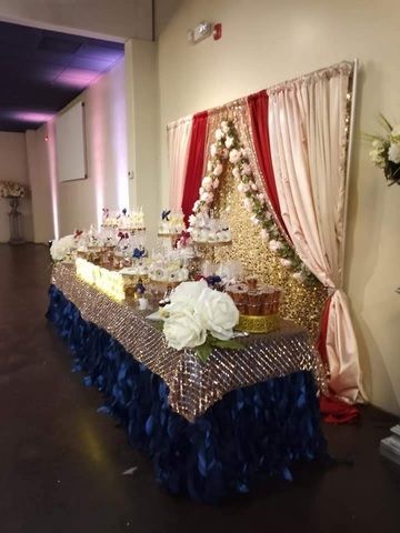 Decorated buffet table with white flowers, gold accents, and red-and-cream drapes in a dim hallway